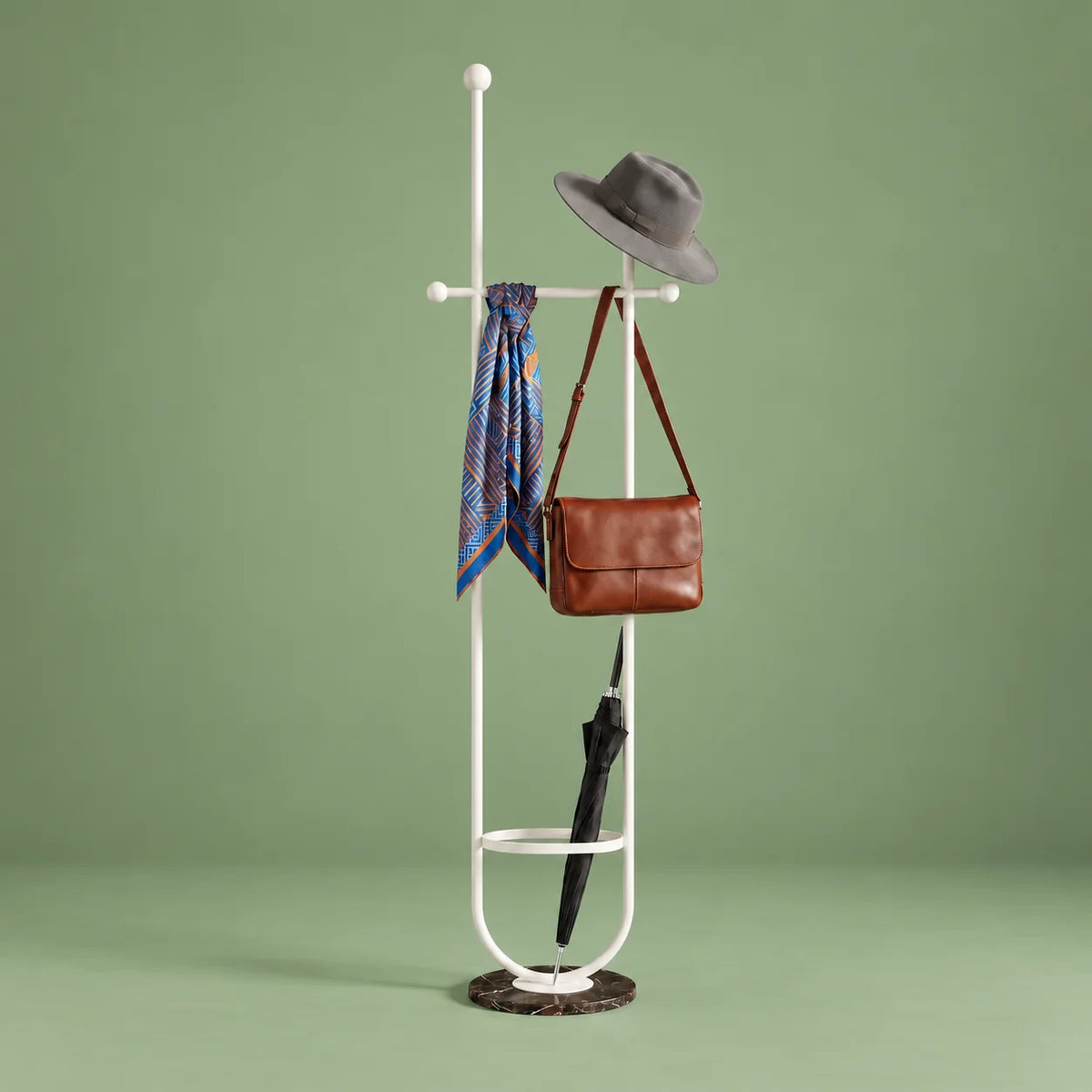 Porte-manteau sur pied en métal blanc avec chapeau, foulard, sac et parapluie, anneau porte-parapluie et base ronde en marbre sombre veiné sur fond vert sauge