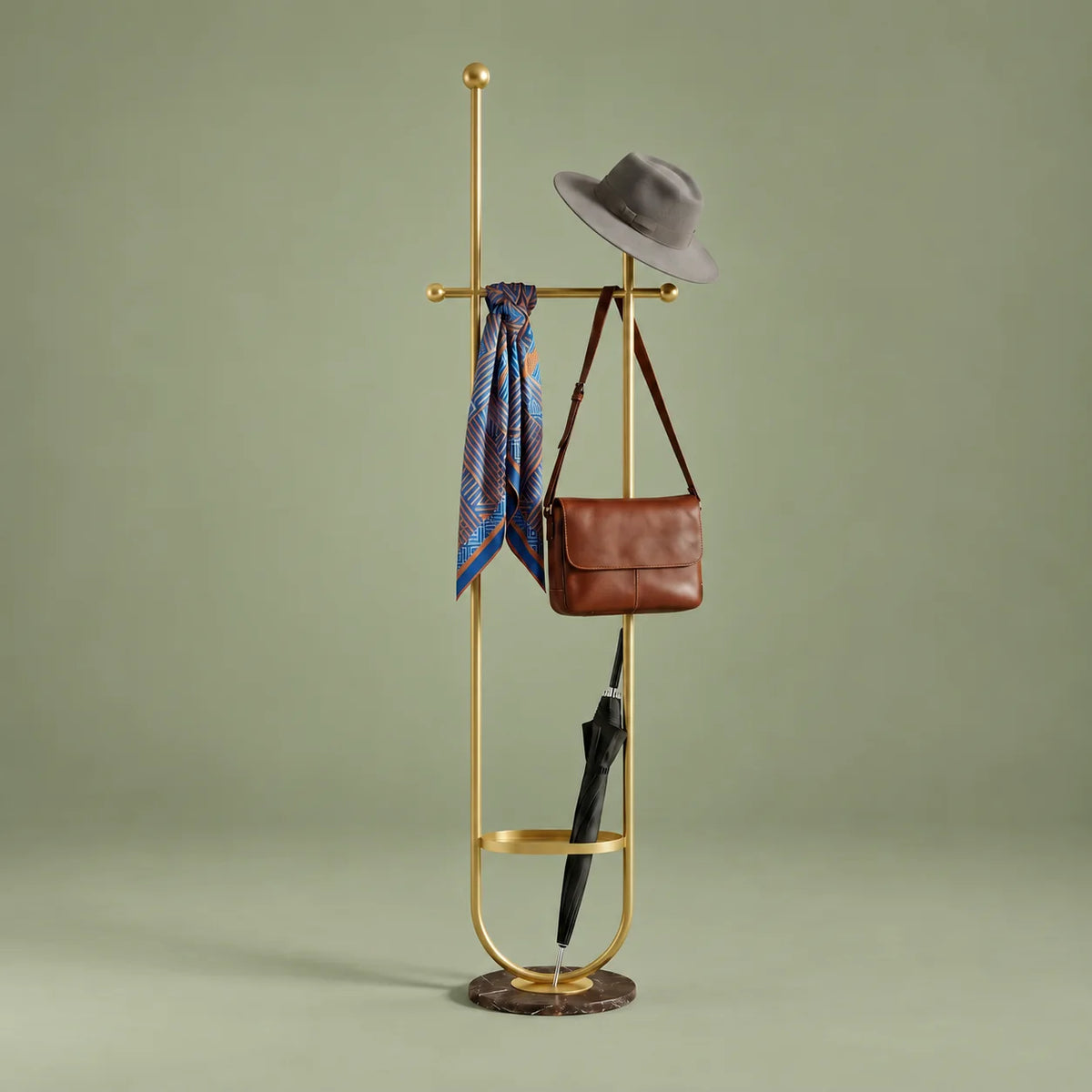 Porte-manteau sur pied en métal doré avec chapeau, foulard, sac et parapluie, anneau porte-parapluie et base ronde sombre sur fond vert sauge