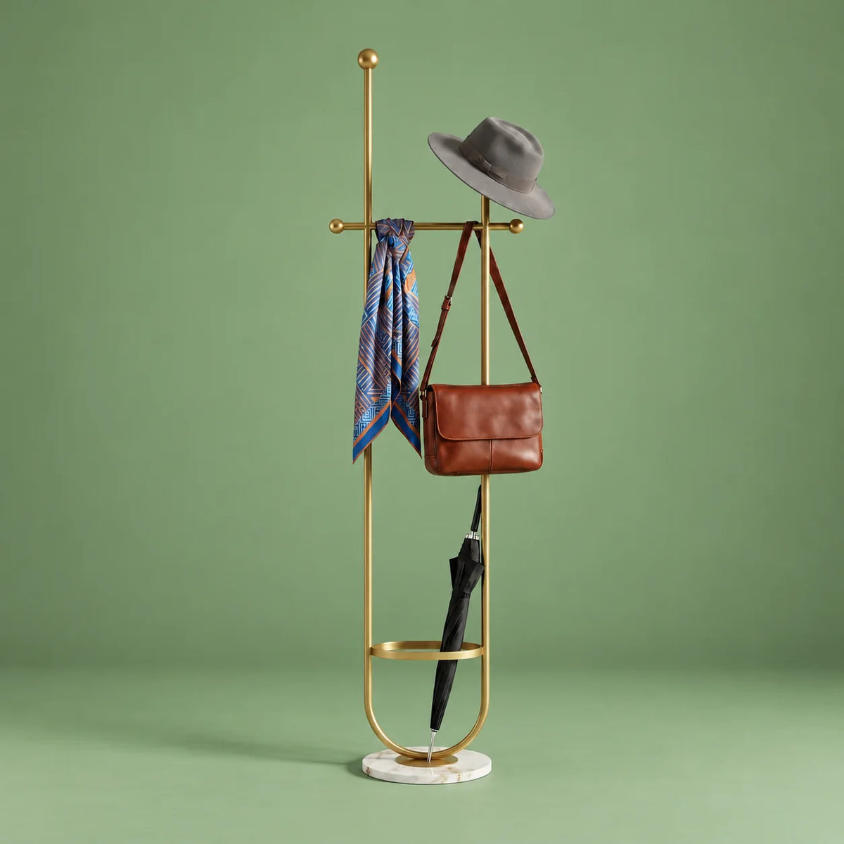 Porte-manteau sur pied en métal doré avec chapeau, foulard, sac et parapluie, anneau porte-parapluie et base ronde en marbre blanc veiné sur fond vert sauge