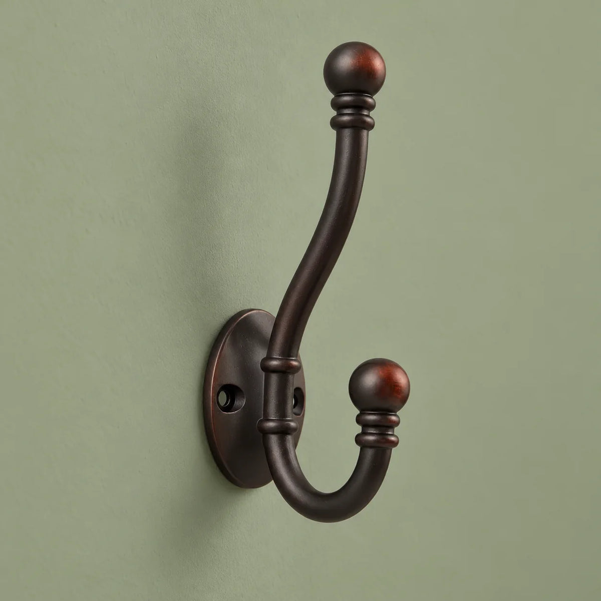 Vue de biais des deux bras de la patère bronze foncé sur fond vert sauge