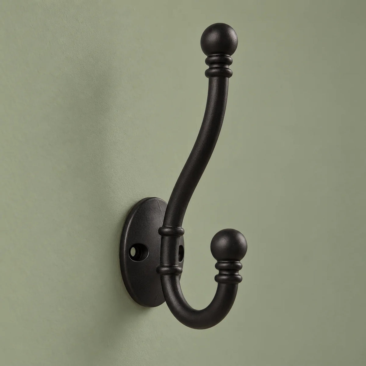 Vue de biais des deux bras courbés de la patère ancienne noire sur fond vert sauge