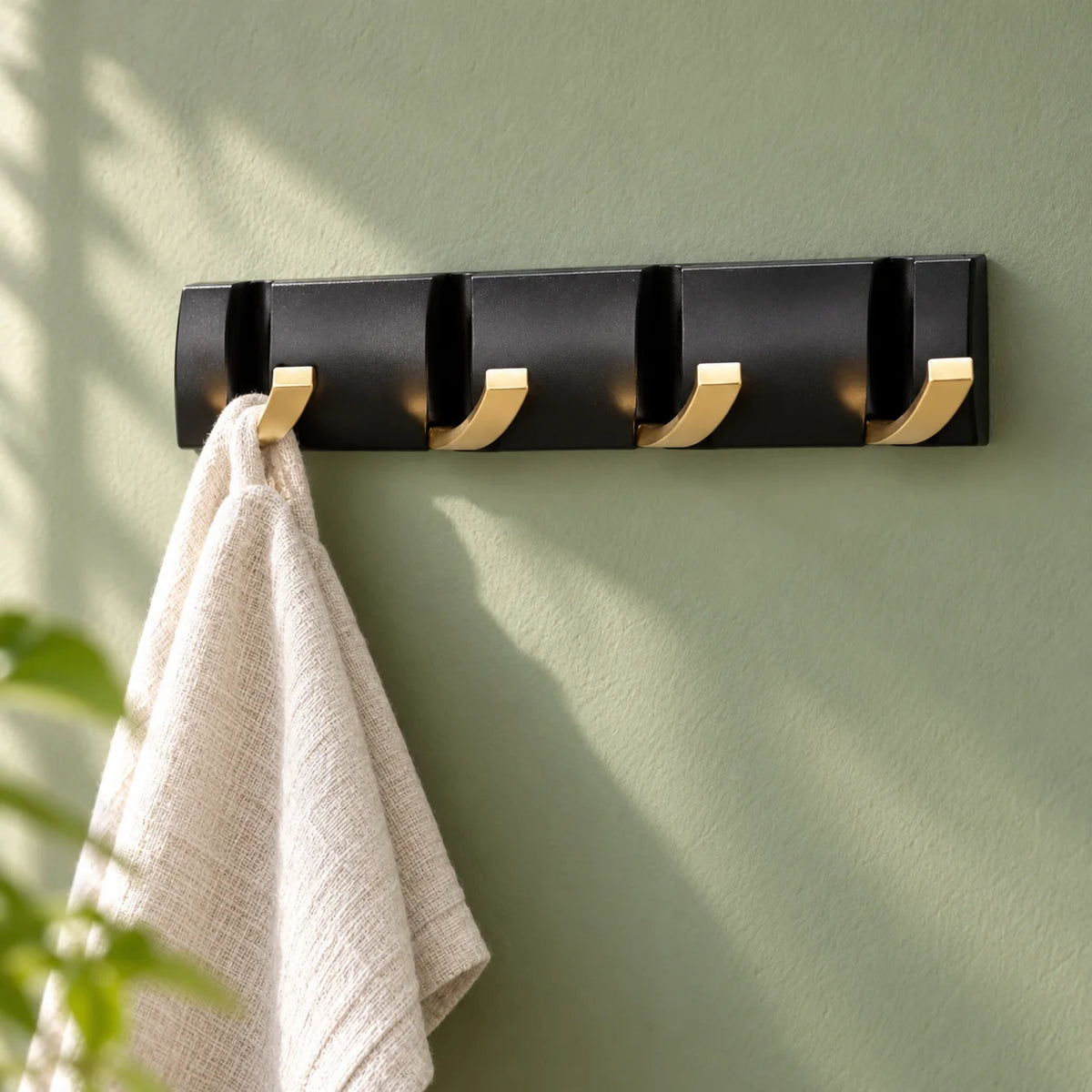 Petit rail noir et doré à quatre crochets avec serviette sur fond vert sauge