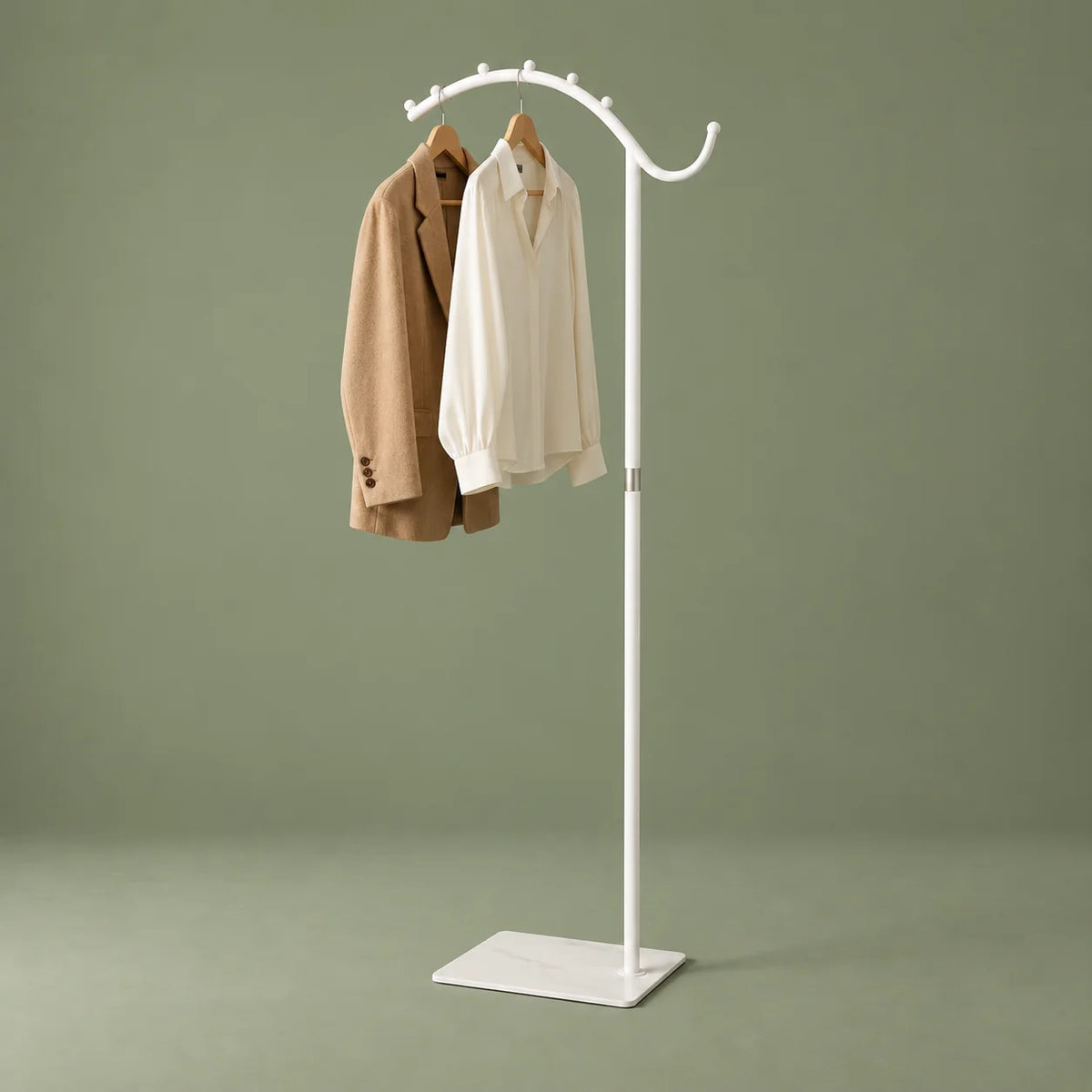 Portant manteau voûté blanc avec veste camel et chemise ivoire sur fond vert sauge