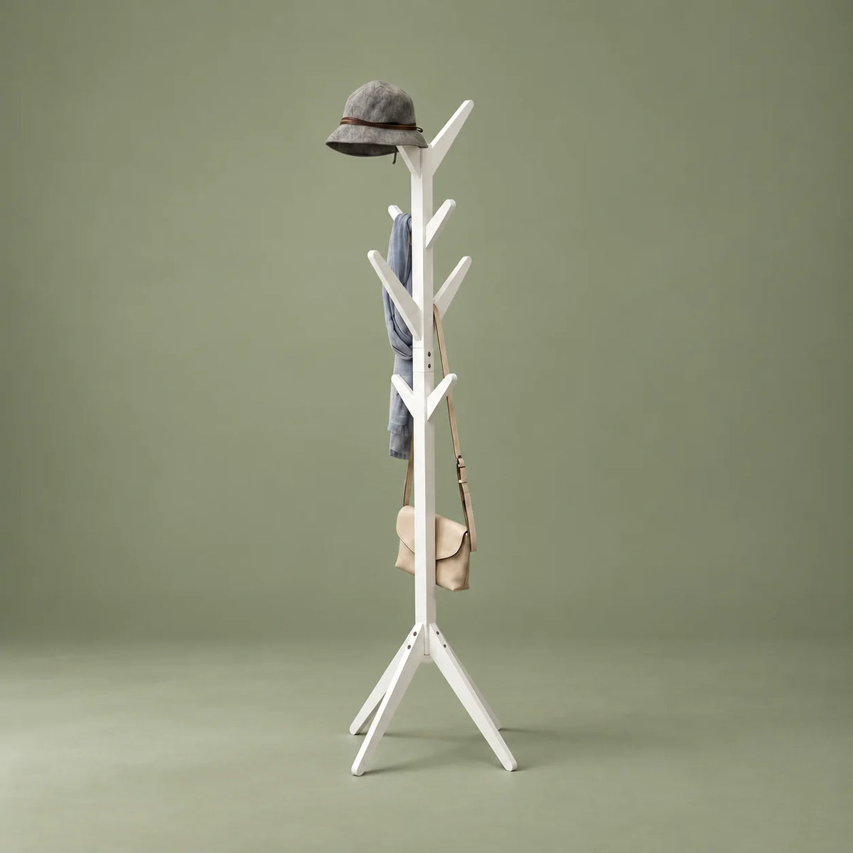 Porte-manteau arbre en bois blanc à pieds évasés, chapeau gris, écharpe et sac beige sur fond vert sauge