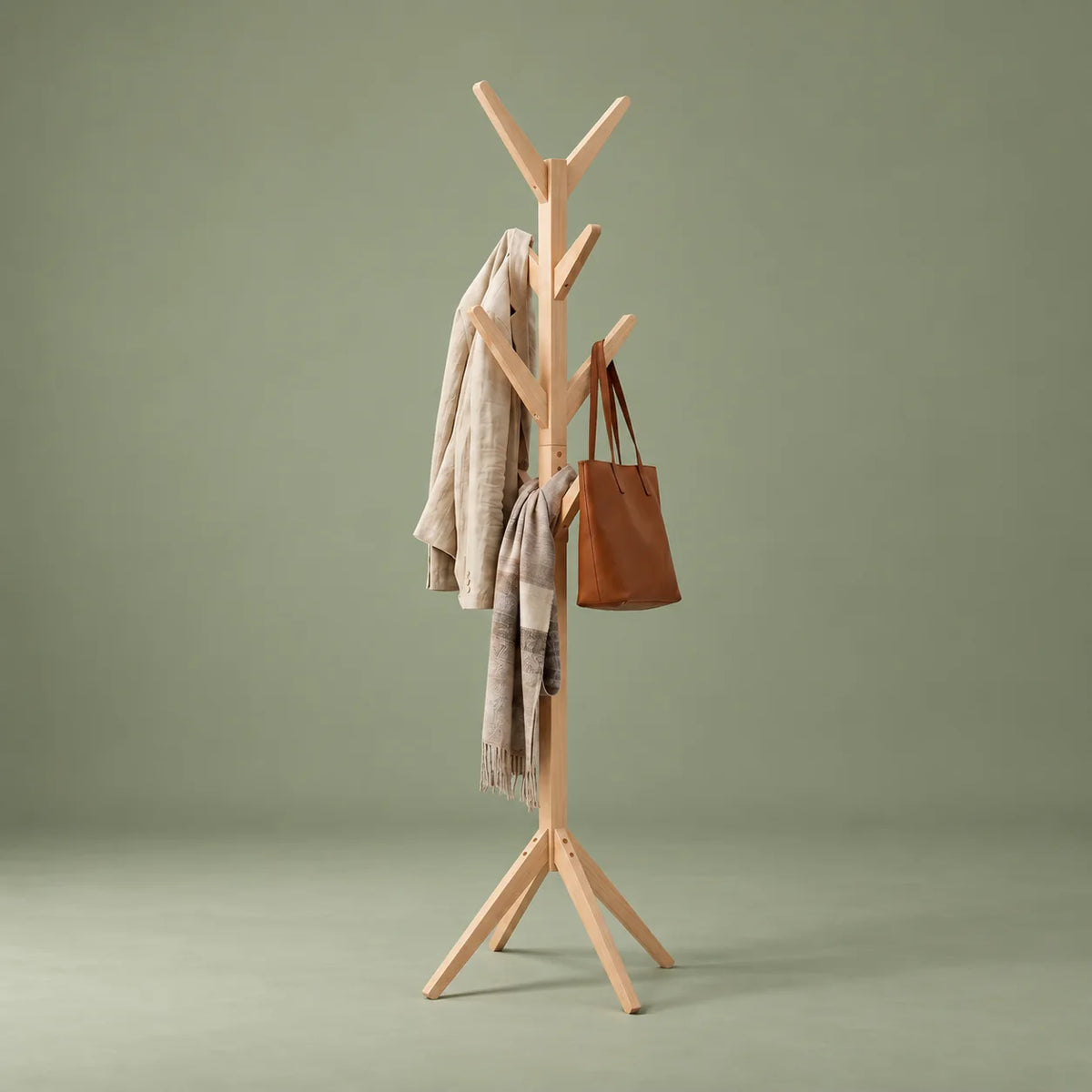 Porte-manteau arbre en bois clair vu de trois quarts droite sur fond vert sauge, avec manteau, écharpe et sac