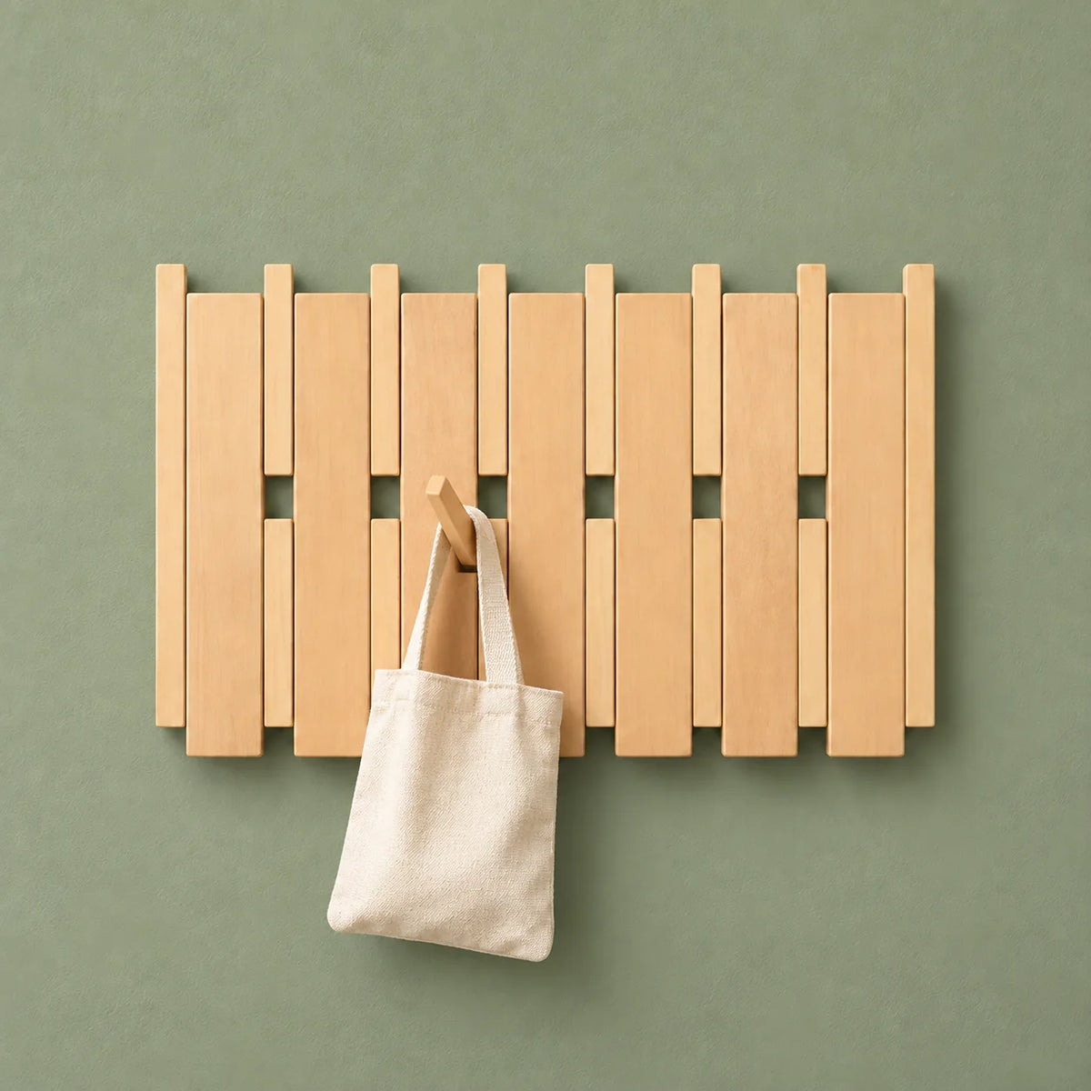 Porte-manteau mural large en bois clair portant un sac en tissu sur fond vert sauge