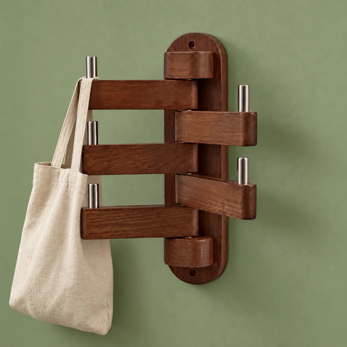 Porte-manteau mural pivotant en bois foncé portant un sac en toile sur fond vert sauge