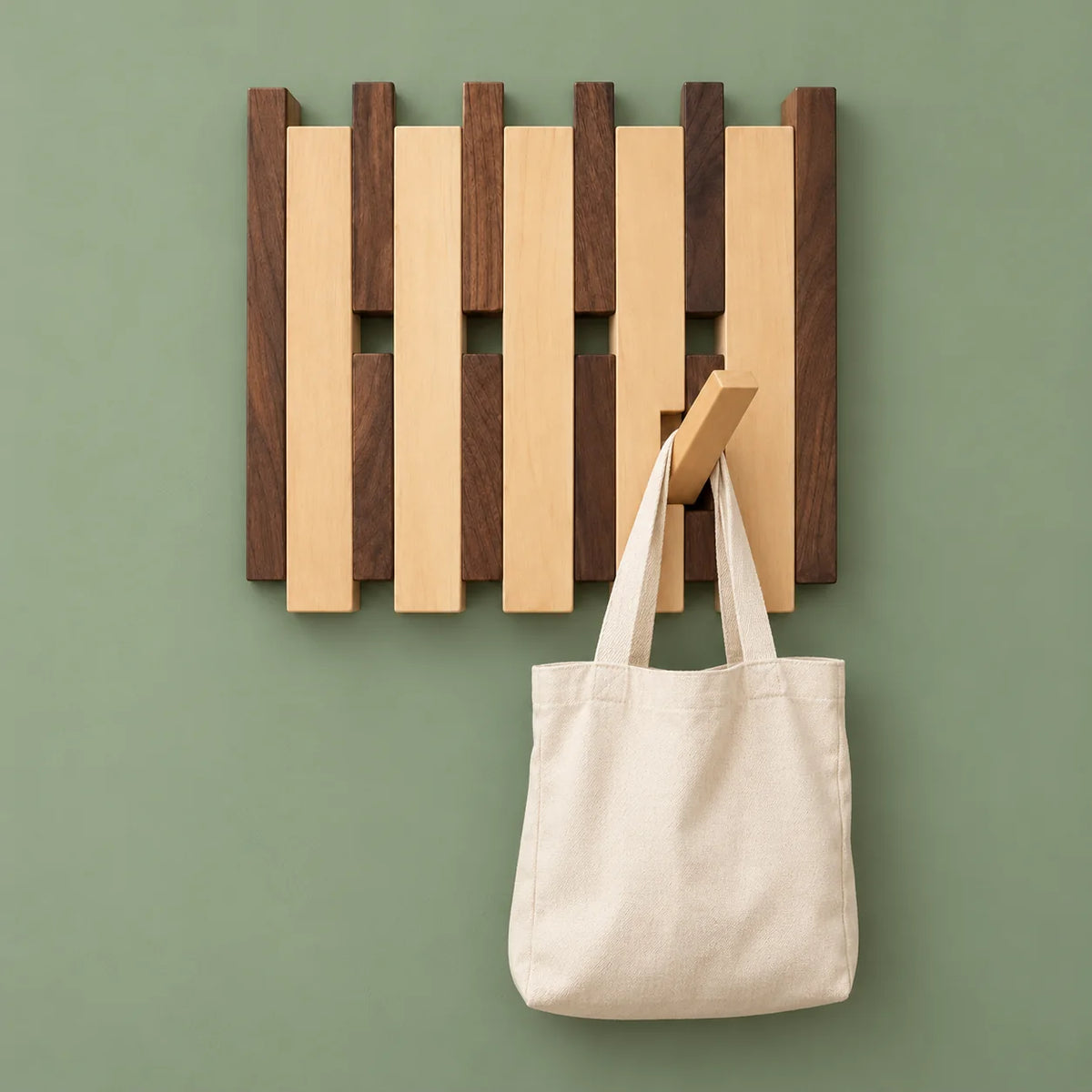 Petit porte-manteau mural bicolore portant un sac en toile sur fond vert sauge