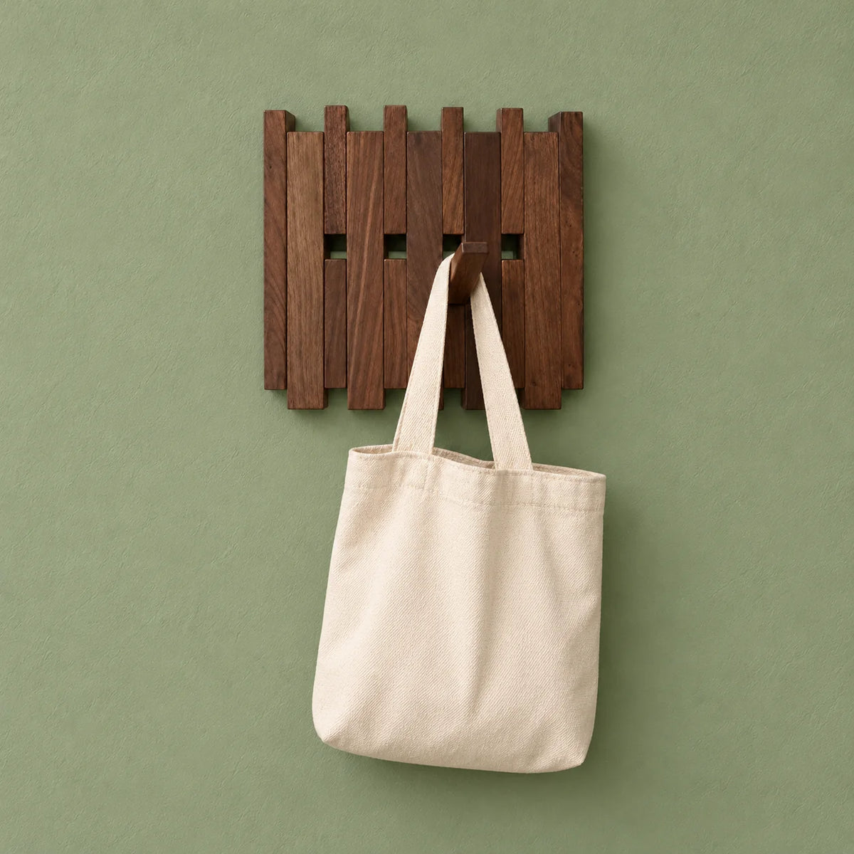 Petit porte-manteau mural en bois foncé portant un sac en tissu sur fond vert sauge