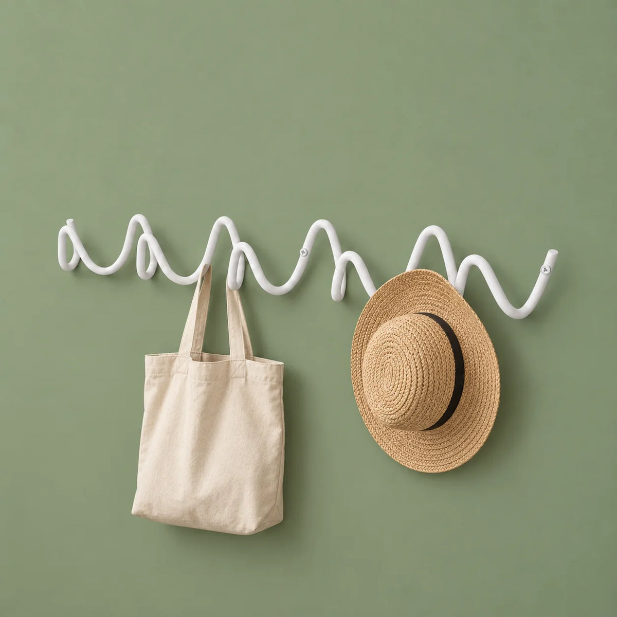 Porte-manteau mural Vrille blanc portant un cabas en toile et un chapeau sur fond vert sauge