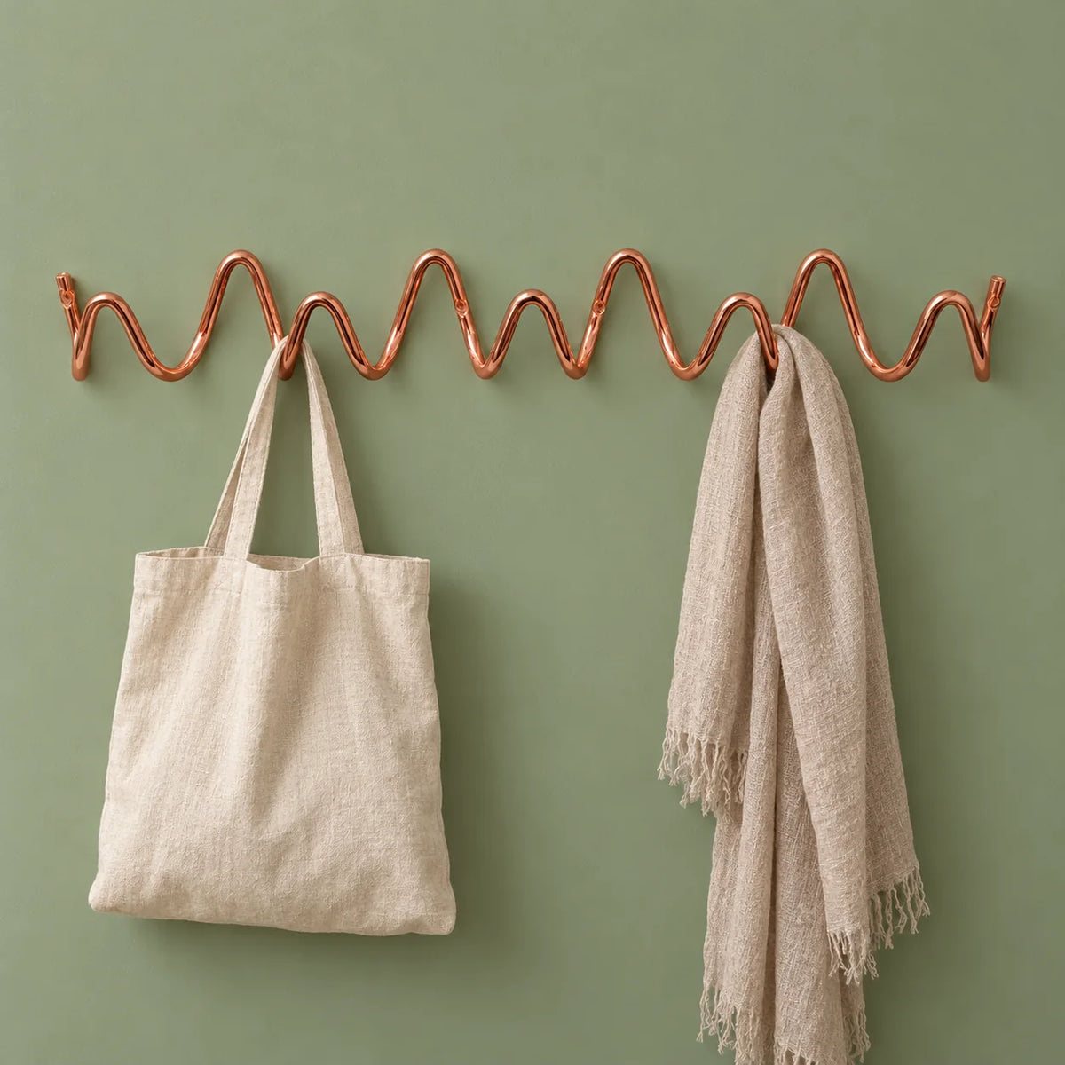 Porte-manteau mural Vrille rose cuivré avec sac en lin et écharpe sur fond vert sauge