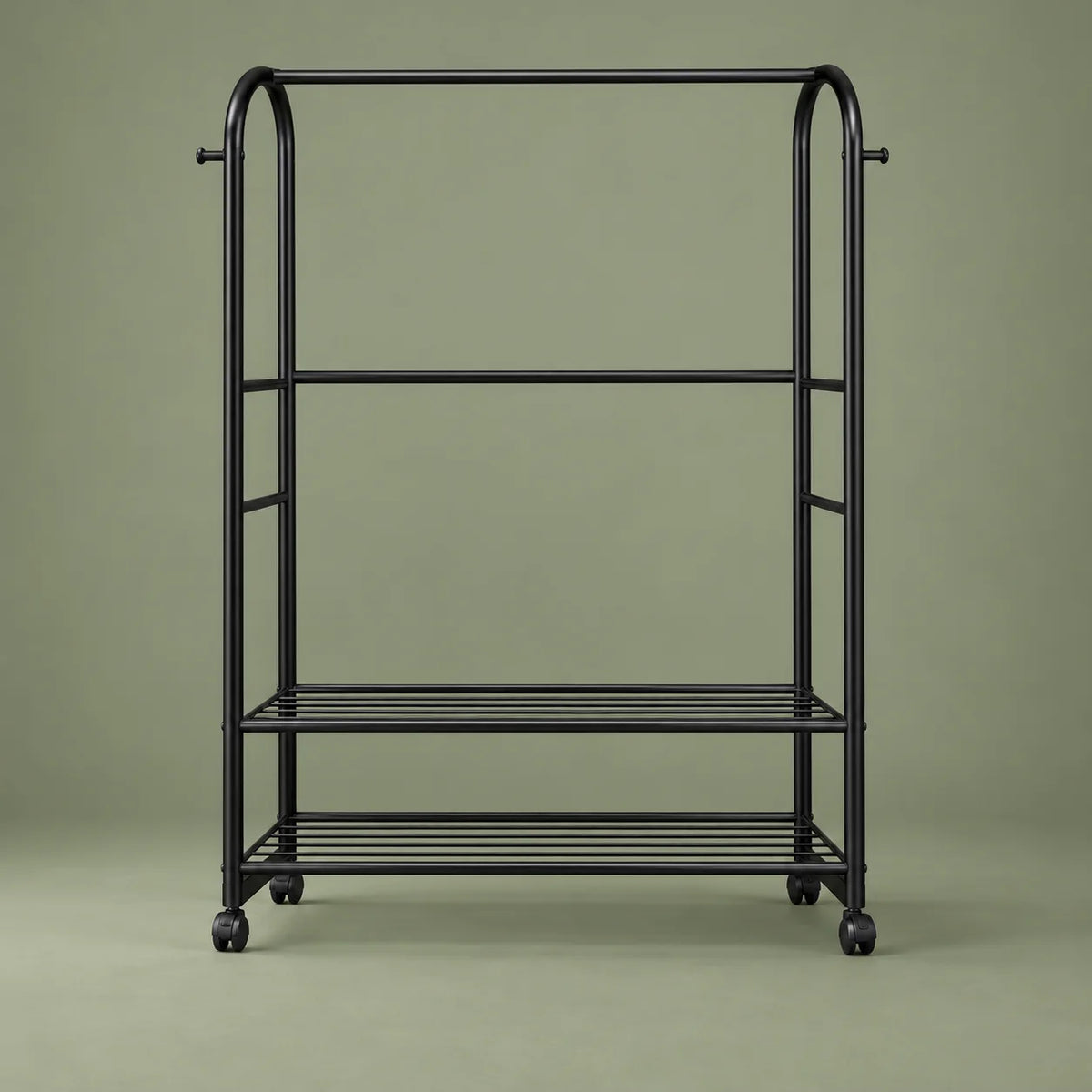 Vue de face du portant noir Luxe, étagères ajourées et roulettes, sur fond vert sauge