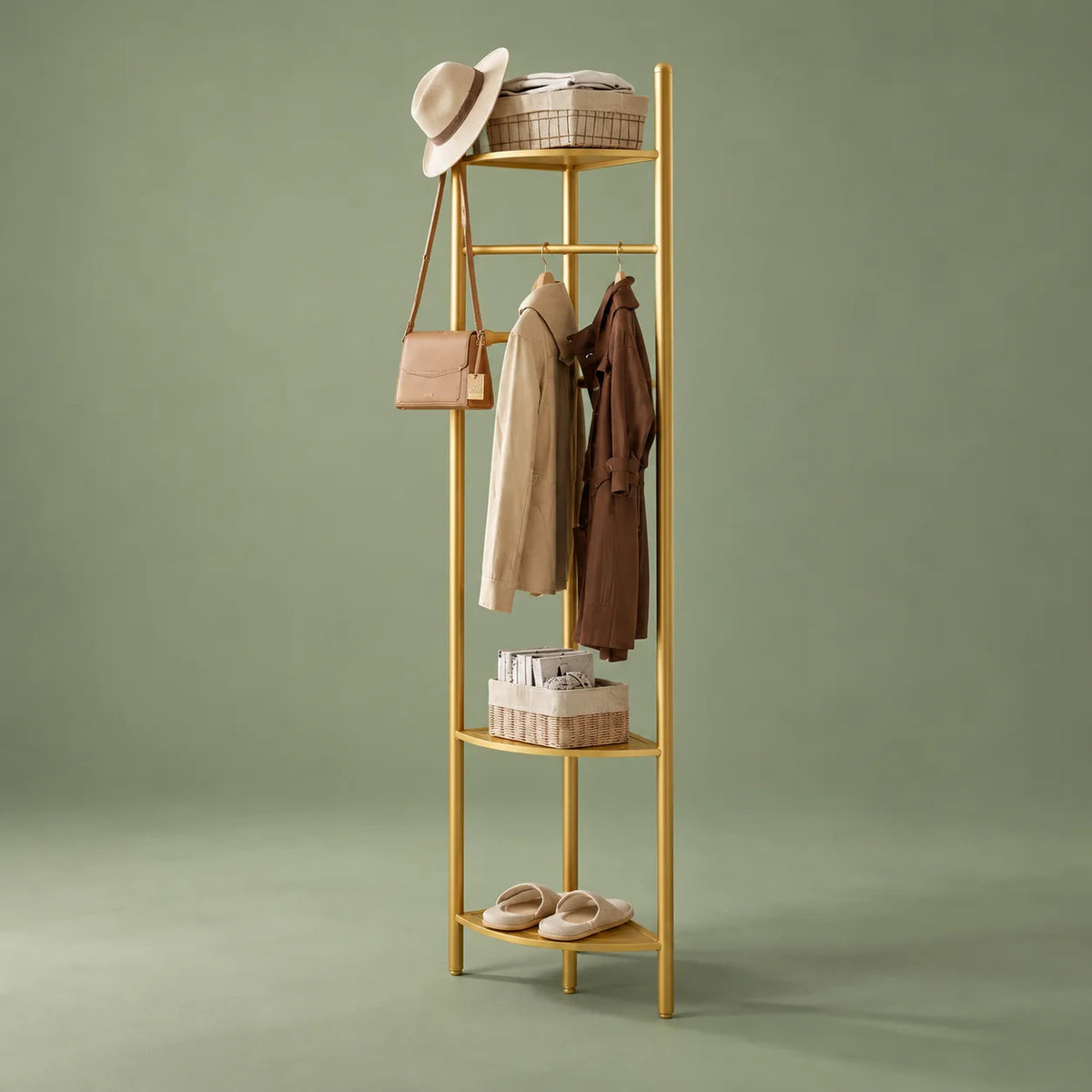 Vue de trois quarts du porte-manteau doré avec manteaux, paniers et chaussures sur fond vert sauge