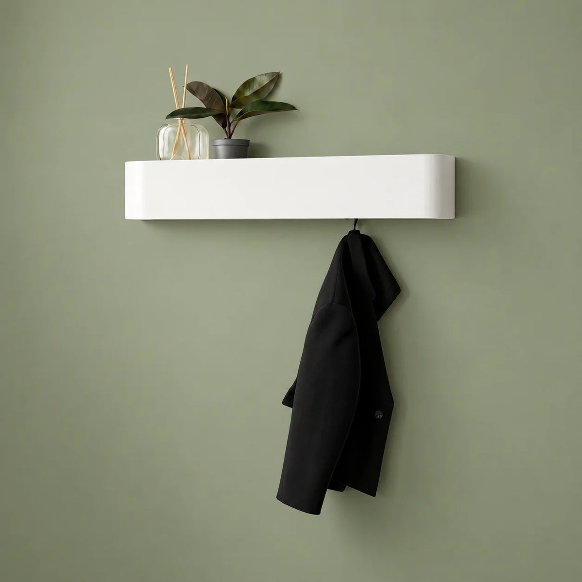 Porte-manteau mural blanc avec plante, diffuseur et manteau noir sur fond vert sauge