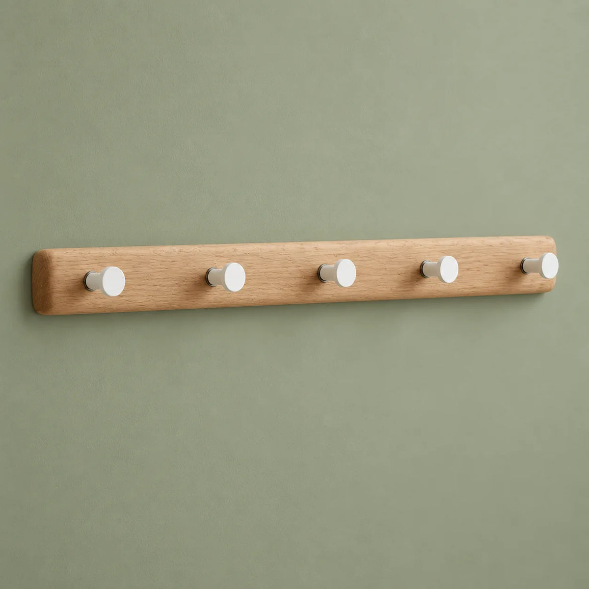 Porte-manteau mural en bois clair à cinq crochets blancs sur fond vert sauge