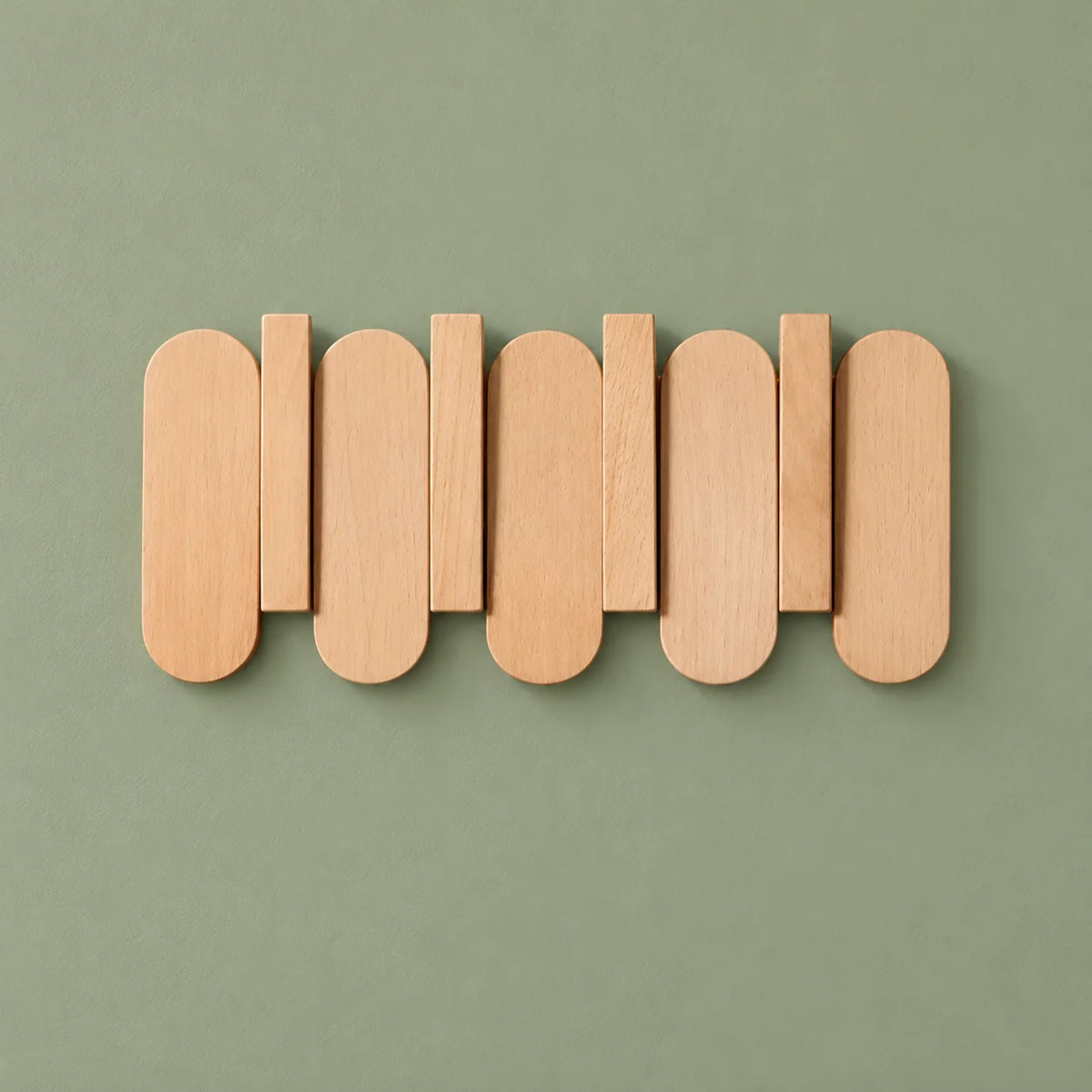 Petit porte-manteau mural en bois clair vu de face sur fond vert sauge