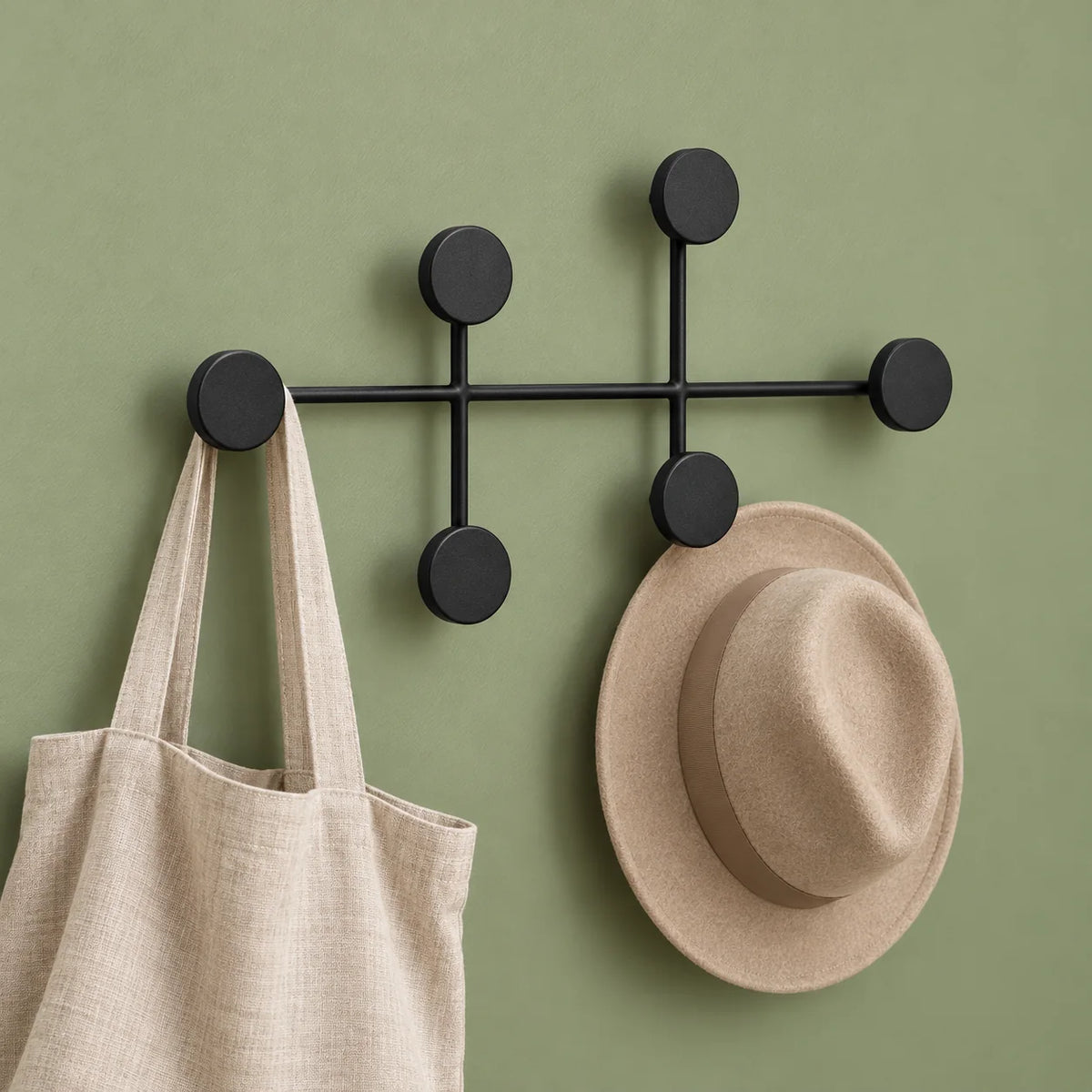 Porte-manteau mural rond noir avec sac en lin et chapeau beige sur mur vert