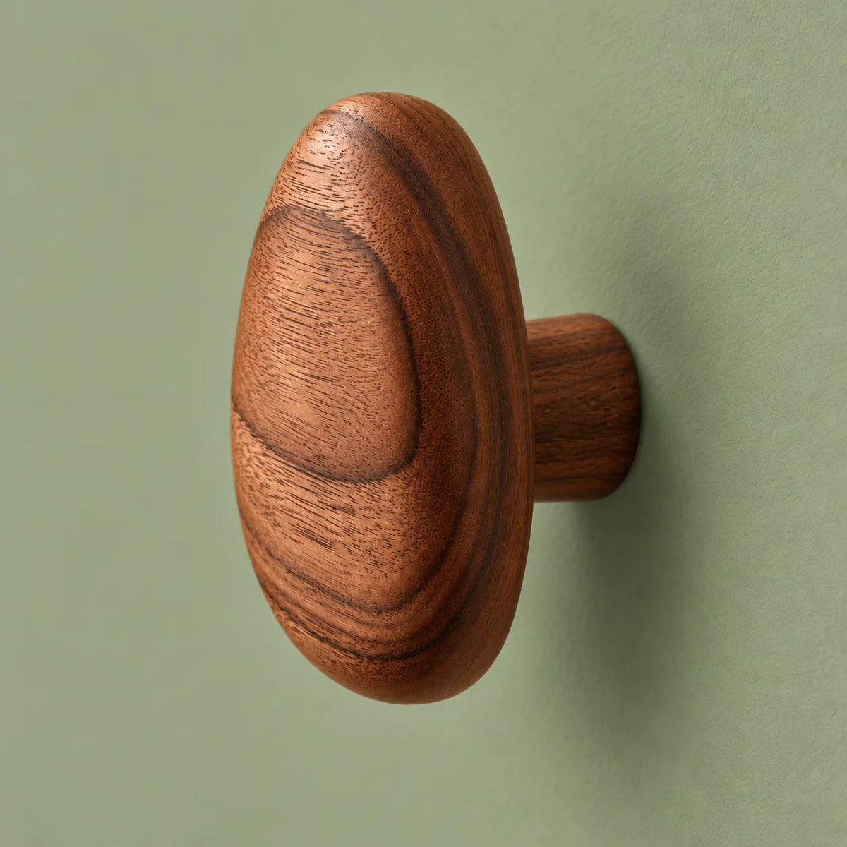 Vue latérale de la patère ovale en bois montrant son relief sur fond vert sauge
