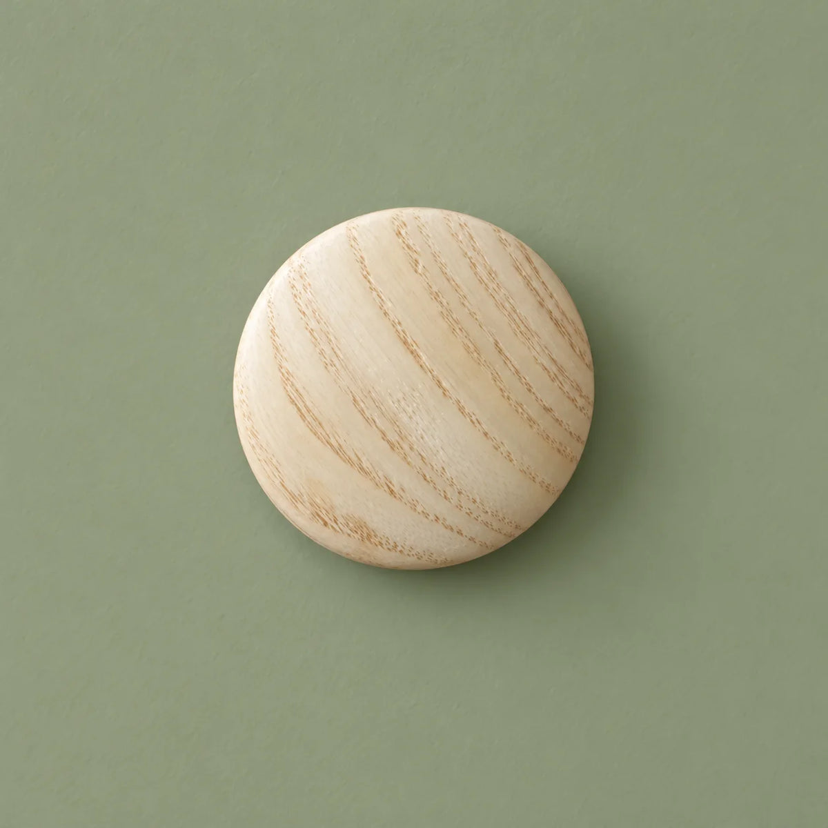 Patère ronde en bois clair vue de face sur fond vert sauge