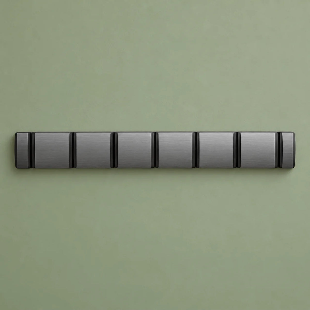 Porte-manteau mural gris en position fermée, crochets rabattus sur fond vert