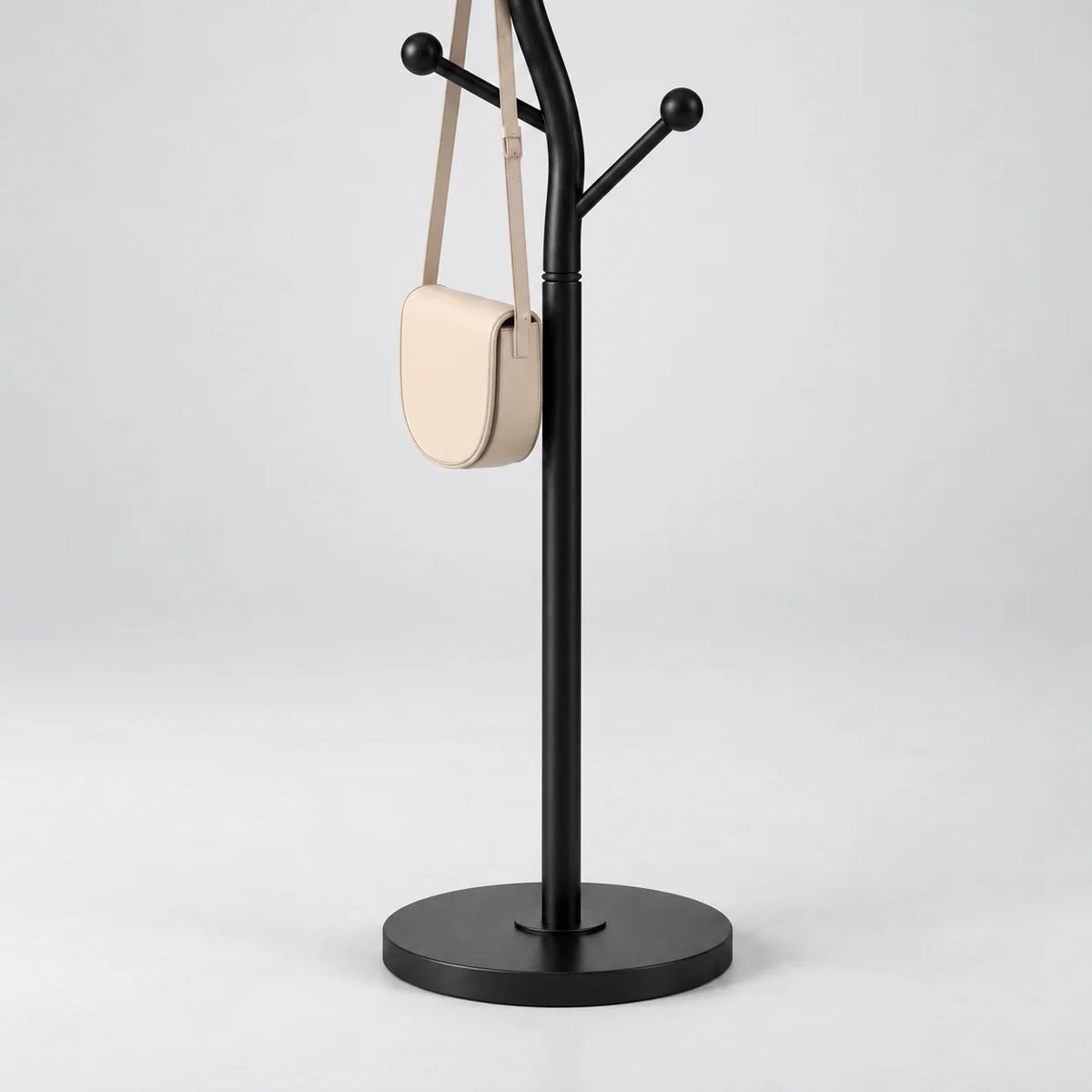 Détail du montant noir mat, du petit sac à bandoulière crème et de la base circulaire noire sur fond gris