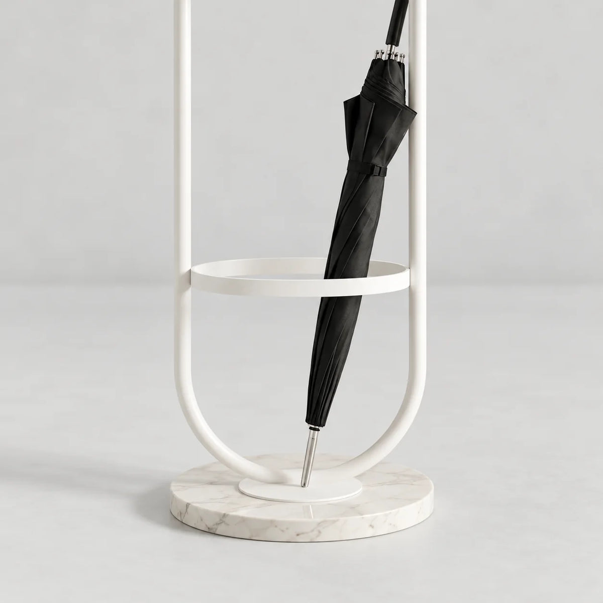 Détail du porte-parapluie en métal blanc, de son anneau circulaire, du parapluie fermé et de la base ronde blanche veinée sur fond gris