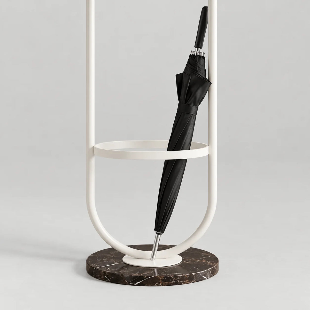 Détail du porte-parapluie en métal blanc, de son anneau circulaire, du parapluie fermé et de la base ronde en marbre sombre veiné sur fond gris