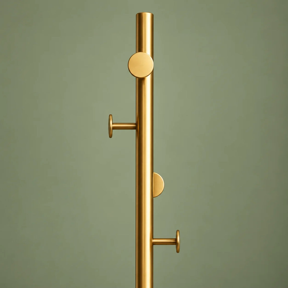 Détail de la partie haute et des crochets du porte-manteau doré sur fond vert