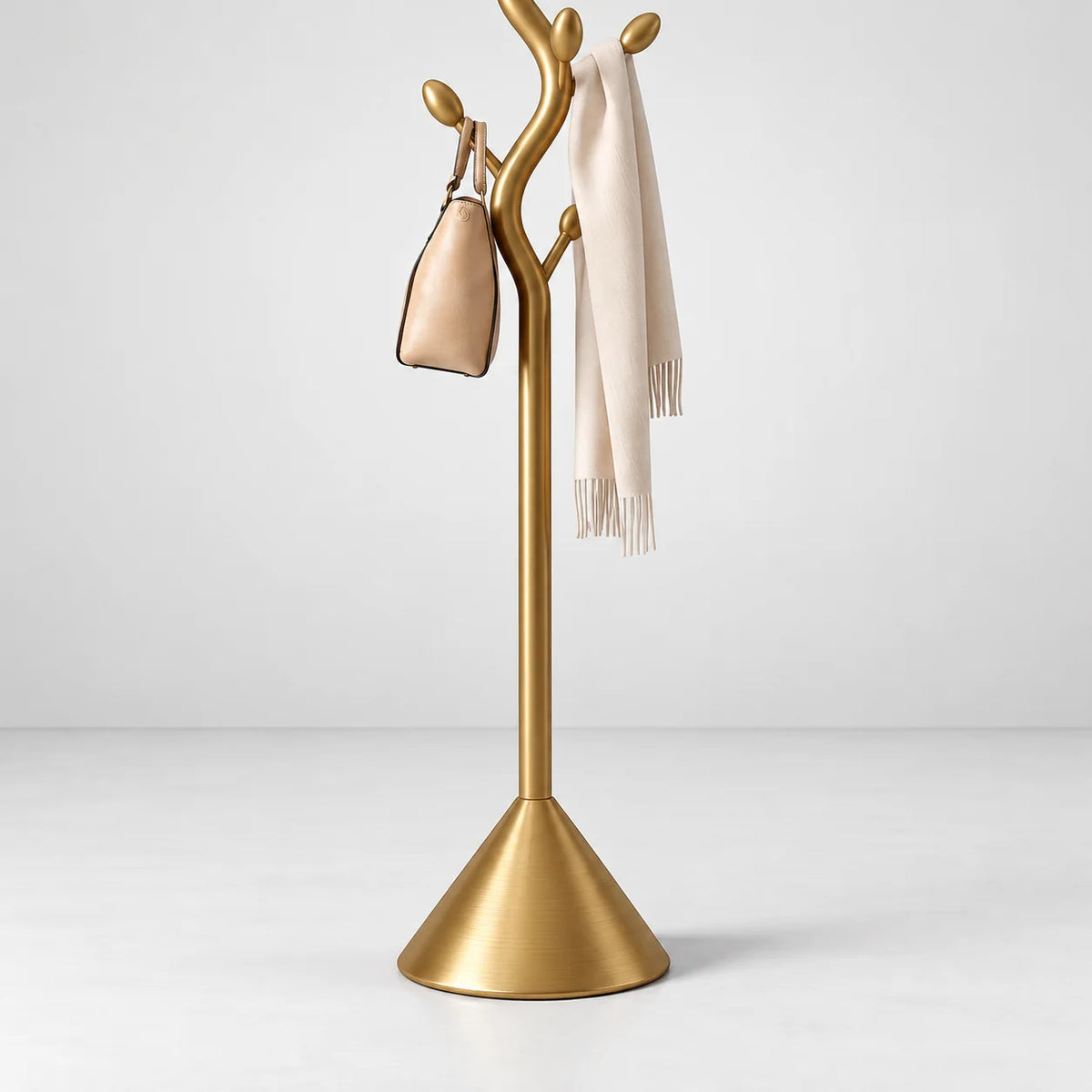 Détail du montant en métal doré, du sac beige, de l’écharpe ivoire et de la large base conique sur fond gris