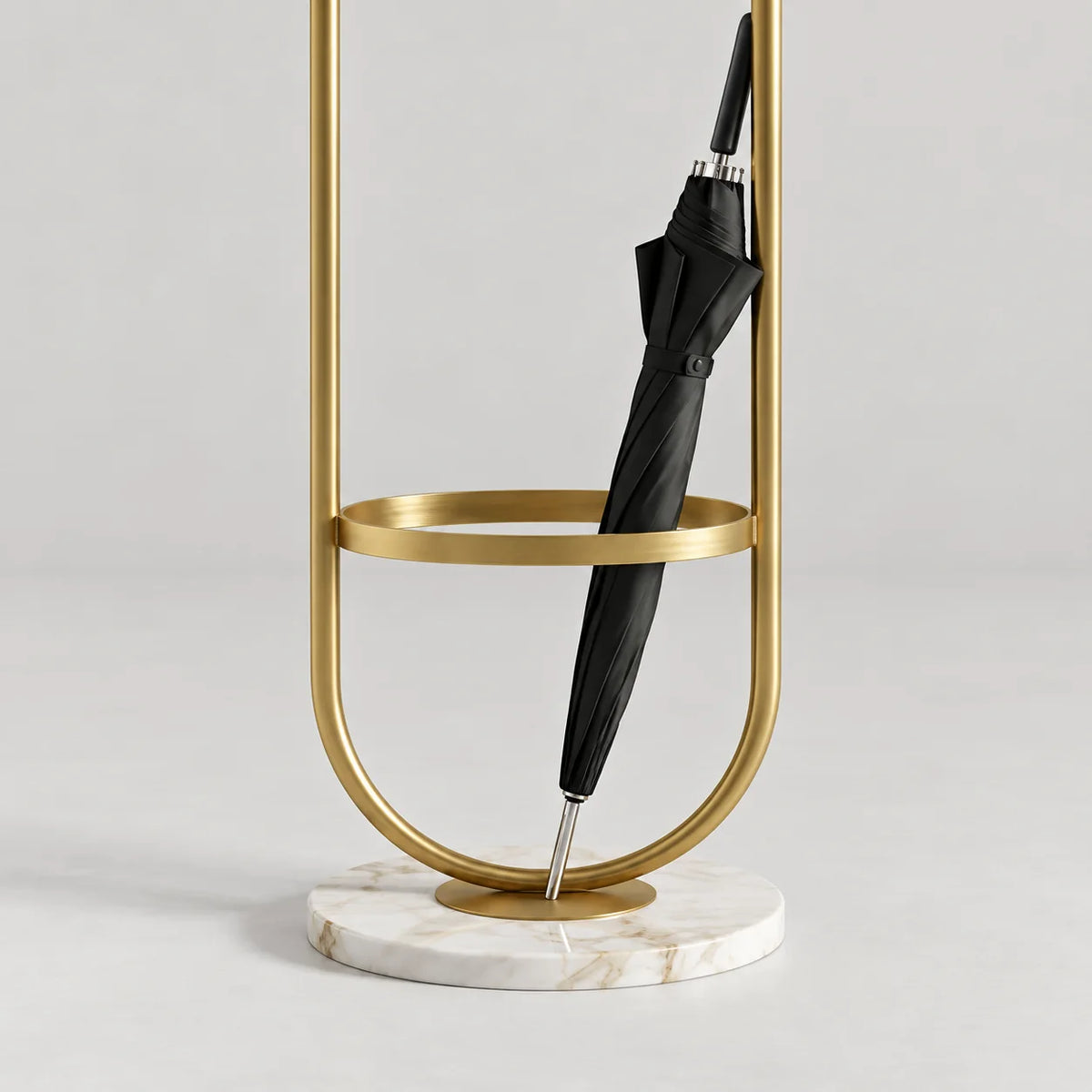 Détail du porte-parapluie en métal doré, de son anneau circulaire, du parapluie fermé et de la base ronde en marbre blanc veiné sur fond gris