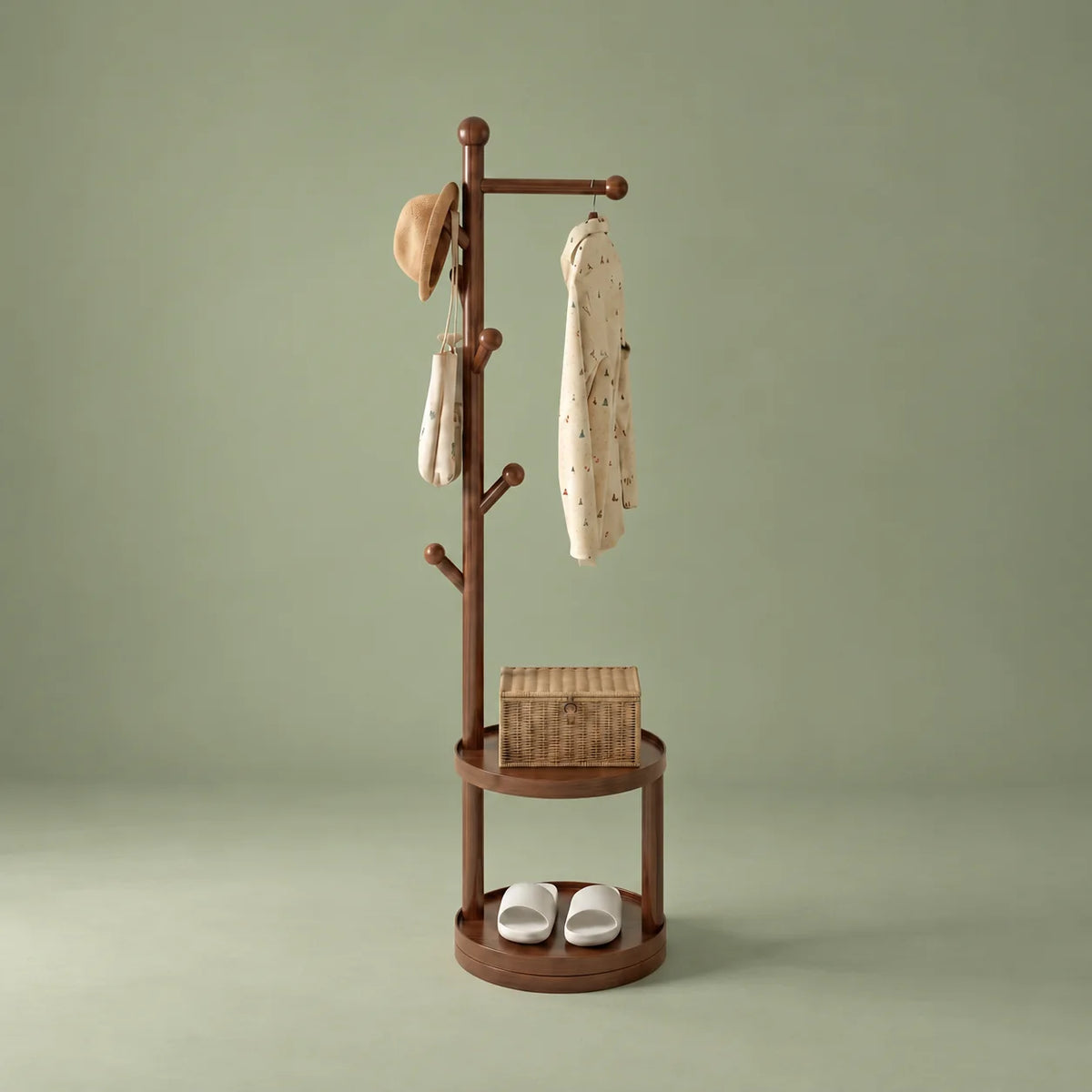 Porte-manteau sur pied en bois marron avec patères, deux étagères rondes, chapeau, sac, vêtement, panier et chaussures sur fond vert sauge