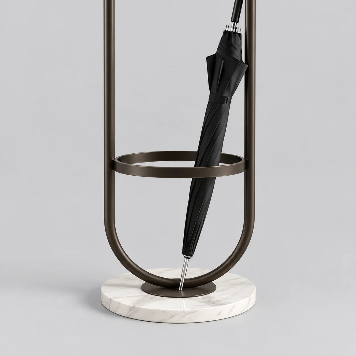 Détail du porte-parapluie en métal noir, de son anneau circulaire, du parapluie fermé et de la base ronde blanche veinée sur fond gris