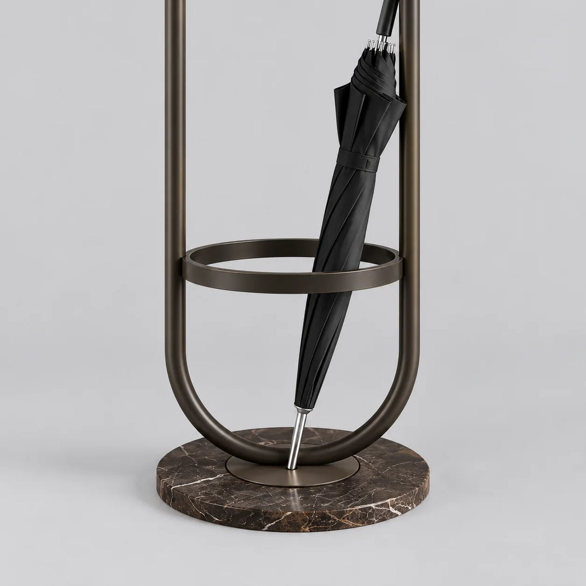 Détail du porte-parapluie en métal noir, de son anneau circulaire, du parapluie fermé et de la base ronde sombre veinée sur fond gris