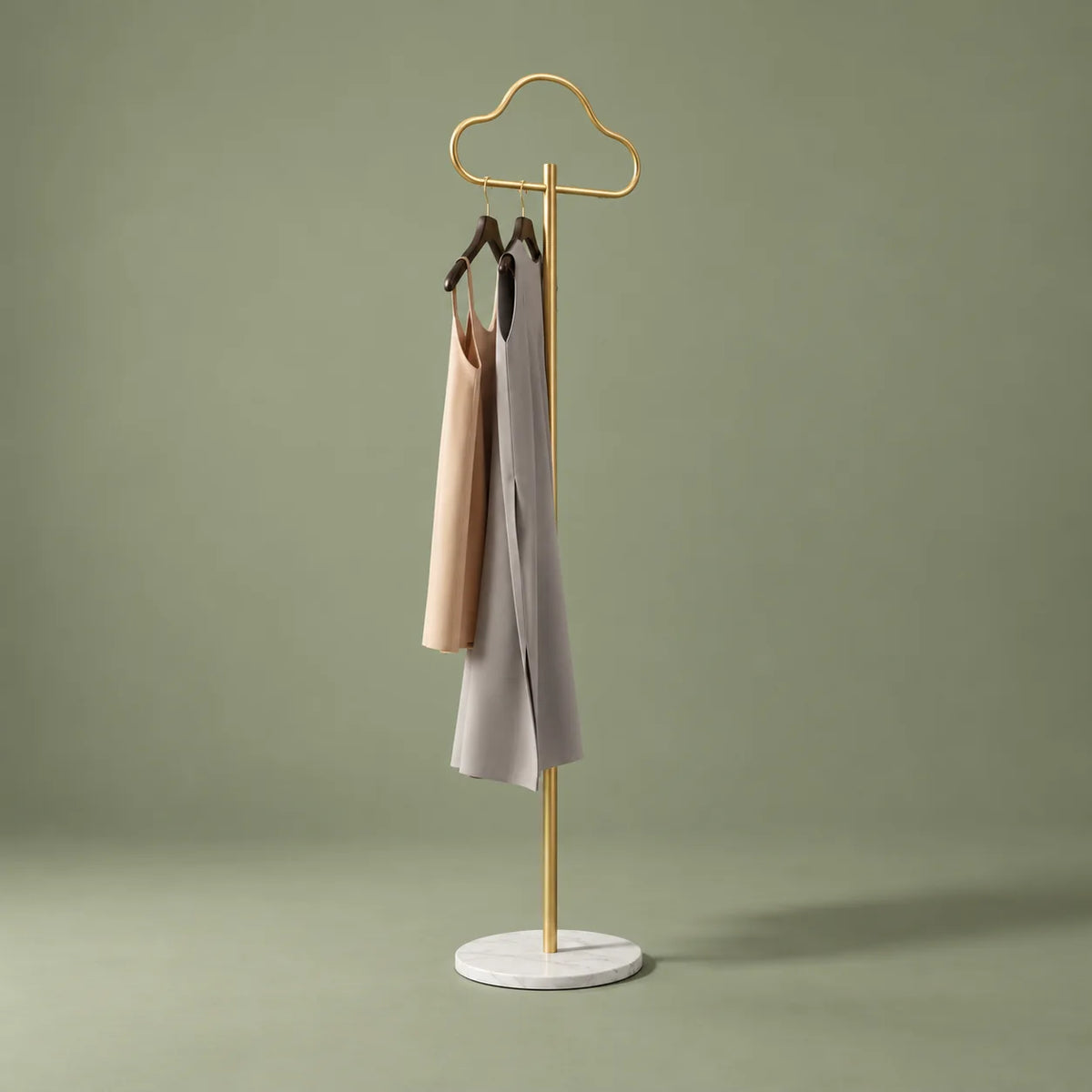 Vue de trois quarts du porte-manteau Nuage d'or doré avec deux vêtements sur fond vert sauge