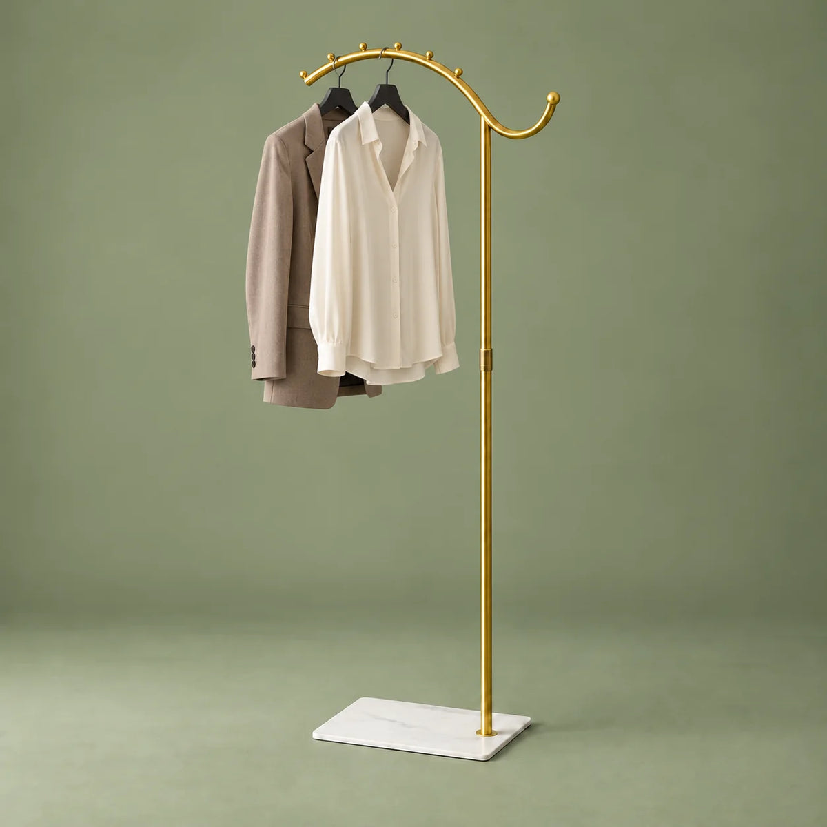 Porte-manteau voûté doré à socle blanc avec chemise ivoire et veste taupe sur fond vert sauge