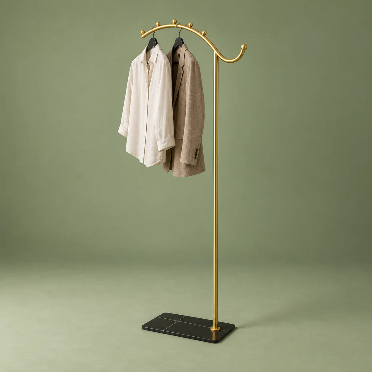 Porte-manteau voûte dorée à socle noir avec chemise ivoire et veste taupe, sur fond vert sauge