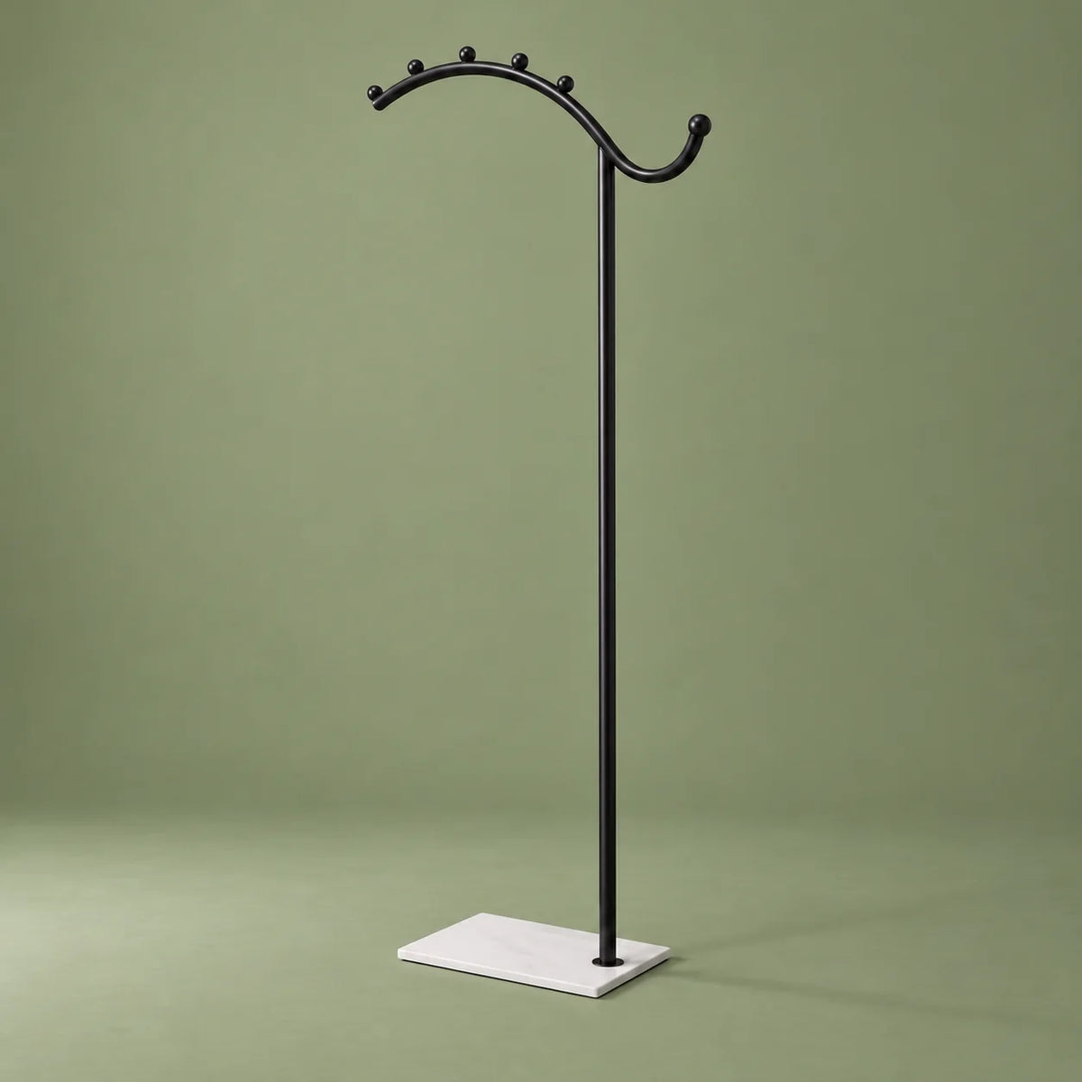 Porte-manteau voûté noir à socle blanc vu légèrement de côté sur fond vert sauge