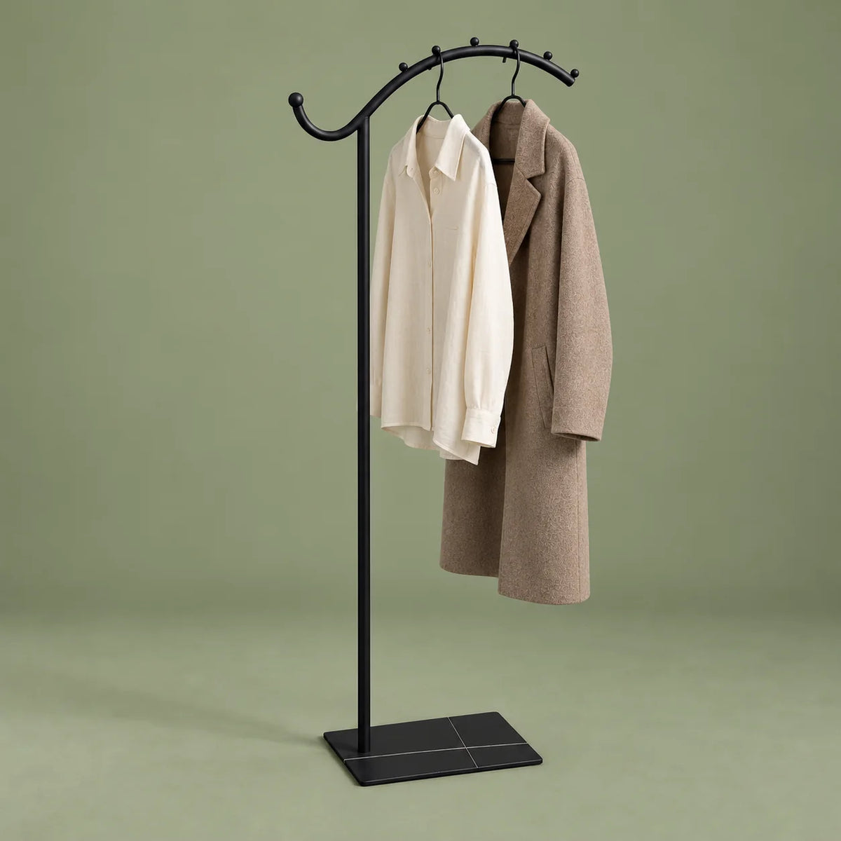 Porte-manteau voûté noir avec chemise ivoire et manteau taupe sur fond vert sauge