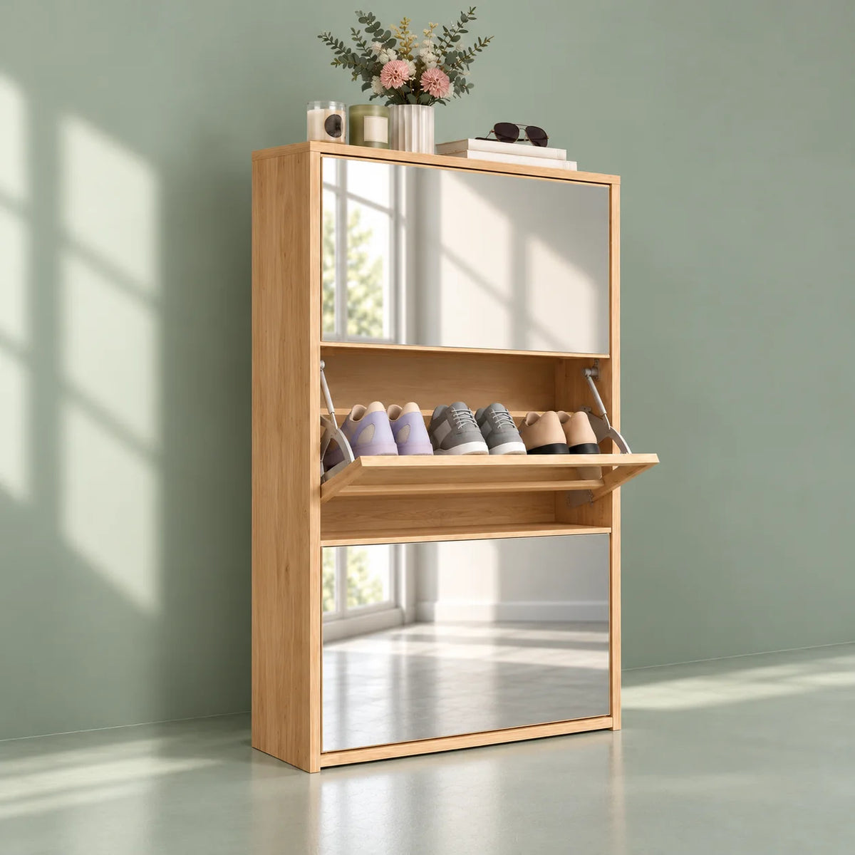 Vue de trois quarts gauche du meuble à chaussures en bois clair avec miroirs sur fond vert sauge