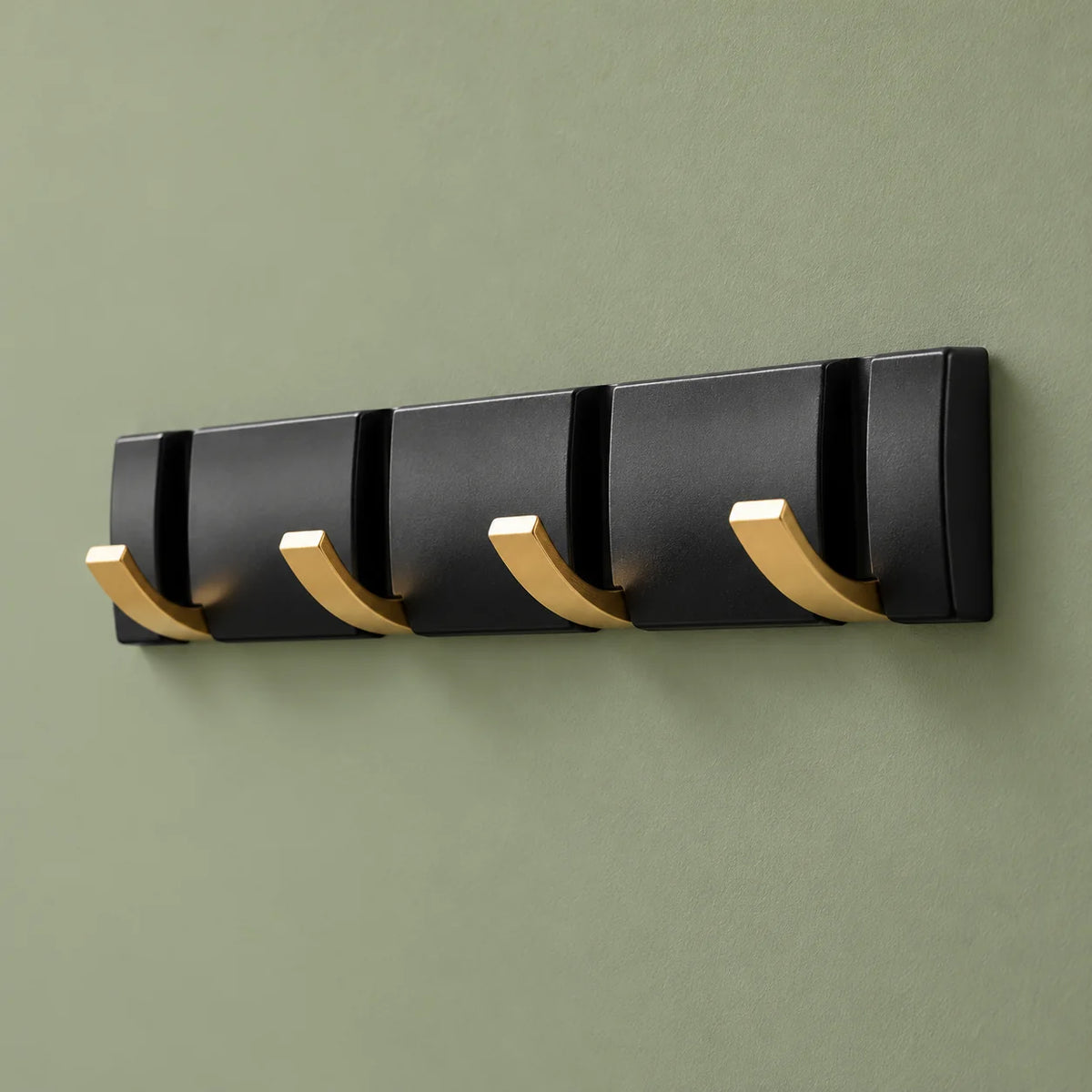 Vue oblique des quatre crochets dorés rabattables sur leur rail noir et fond vert sauge