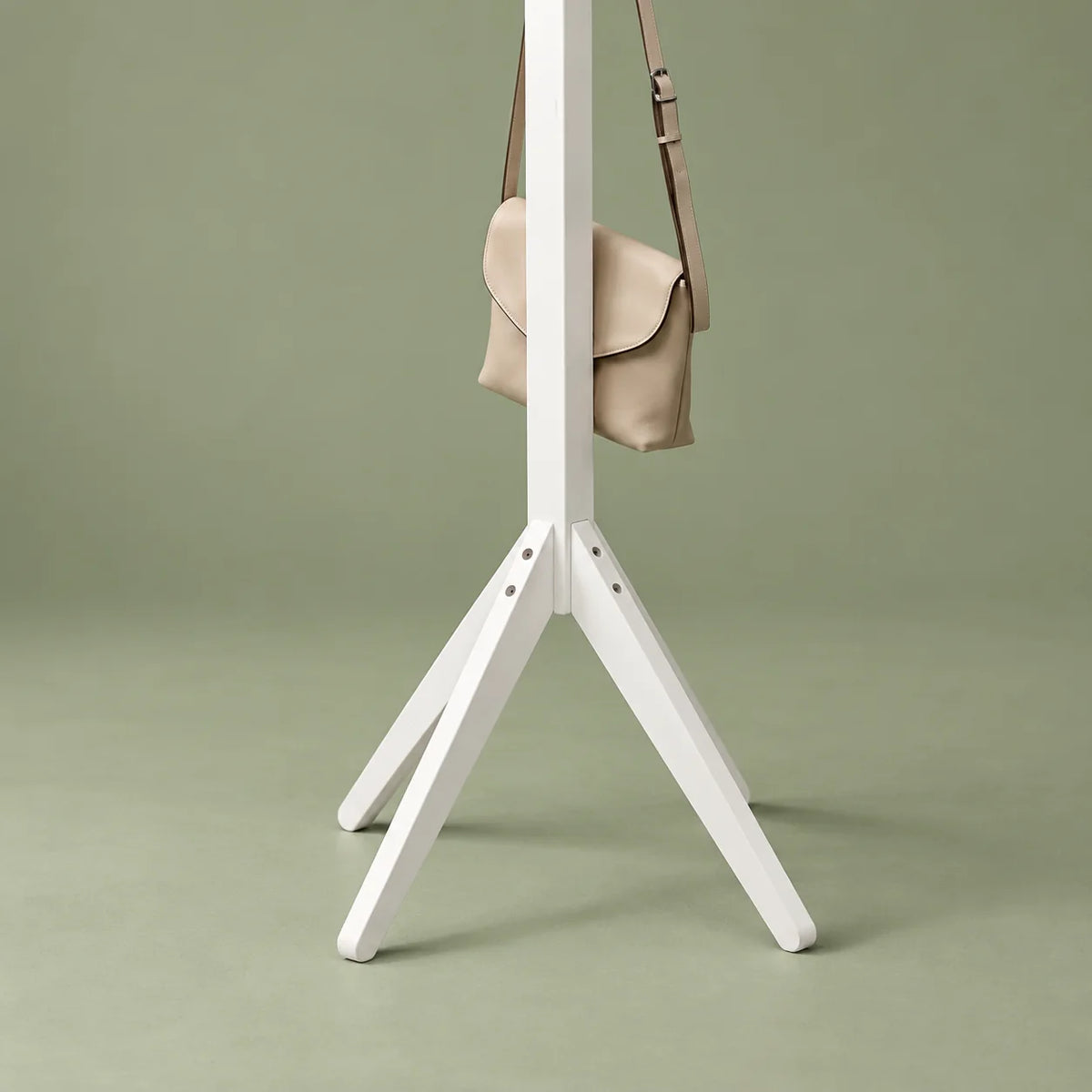 Gros plan sur le piètement évasé en bois blanc et ses fixations, avec sac beige, sur fond vert sauge