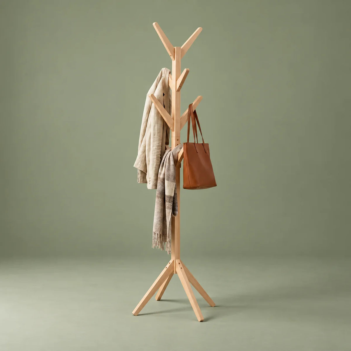 Porte-manteau arbre en bois clair vu de trois quarts gauche sur fond vert sauge, avec manteau, écharpe et sac
