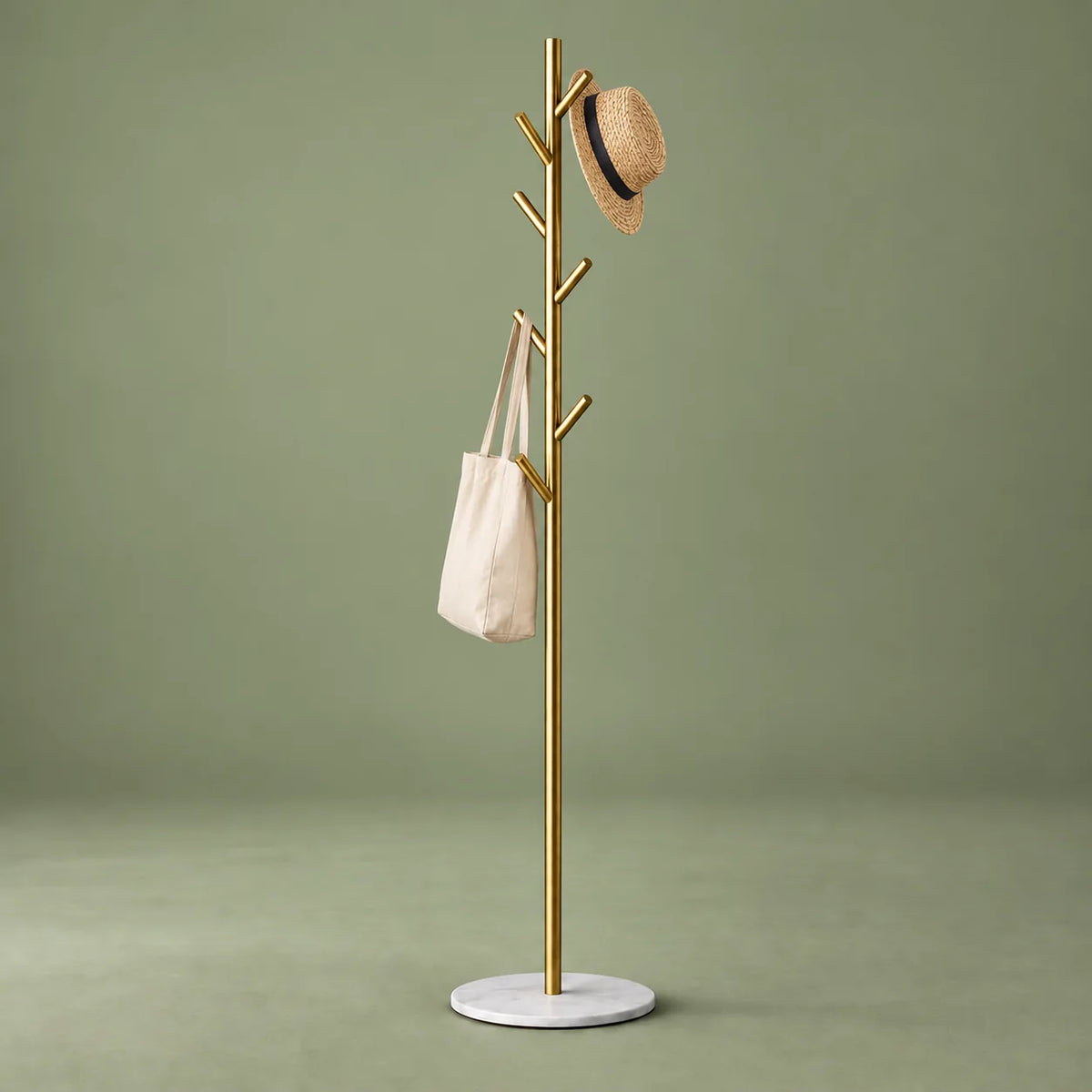 Porte-manteau arbre doré sur pied blanc avec chapeau et sac sur fond vert sauge