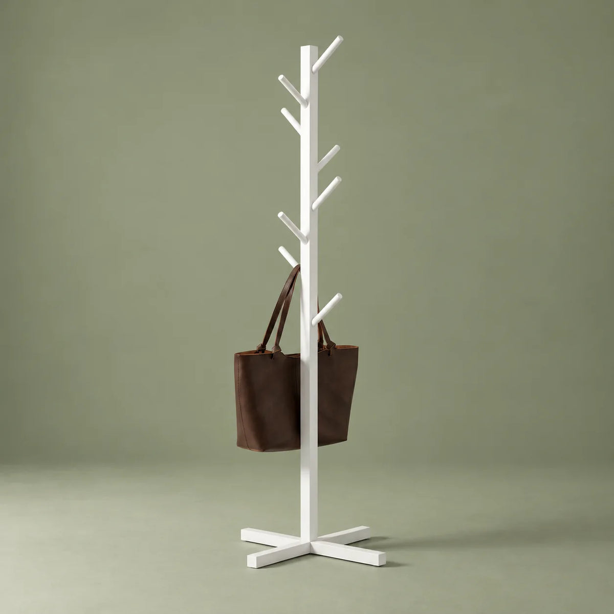 Vue complémentaire du porte-manteau blanc à branches alternées et base croisée avec cabas brun sur fond vert sauge