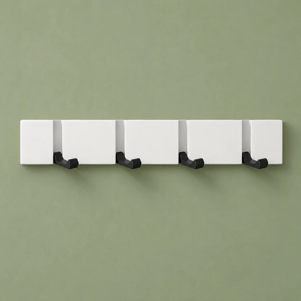 Vue de face du porte-manteau mural blanc à quatre crochets rabattables sur fond vert sauge