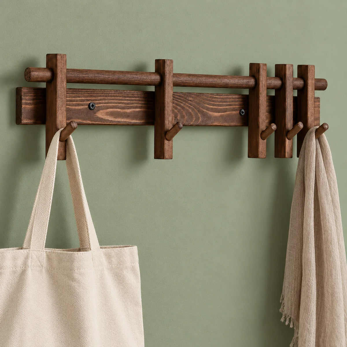 Porte-manteau mural marron avec sac en toile et écharpe sur mur vert sauge