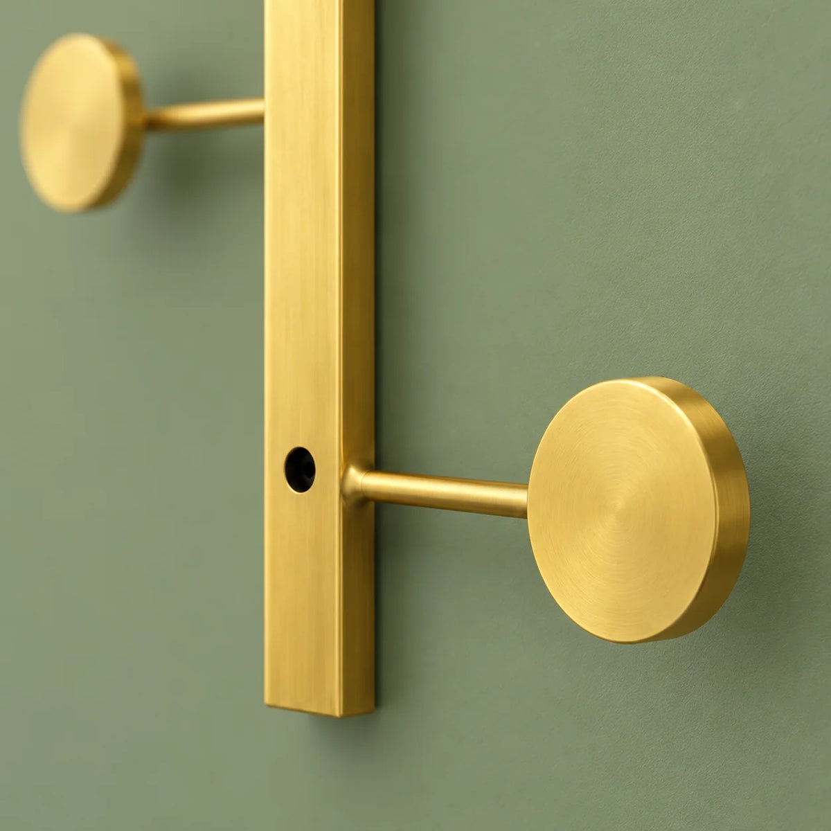 Détail du crochet inférieur rond et de sa tige en métal doré sur fond vert sauge