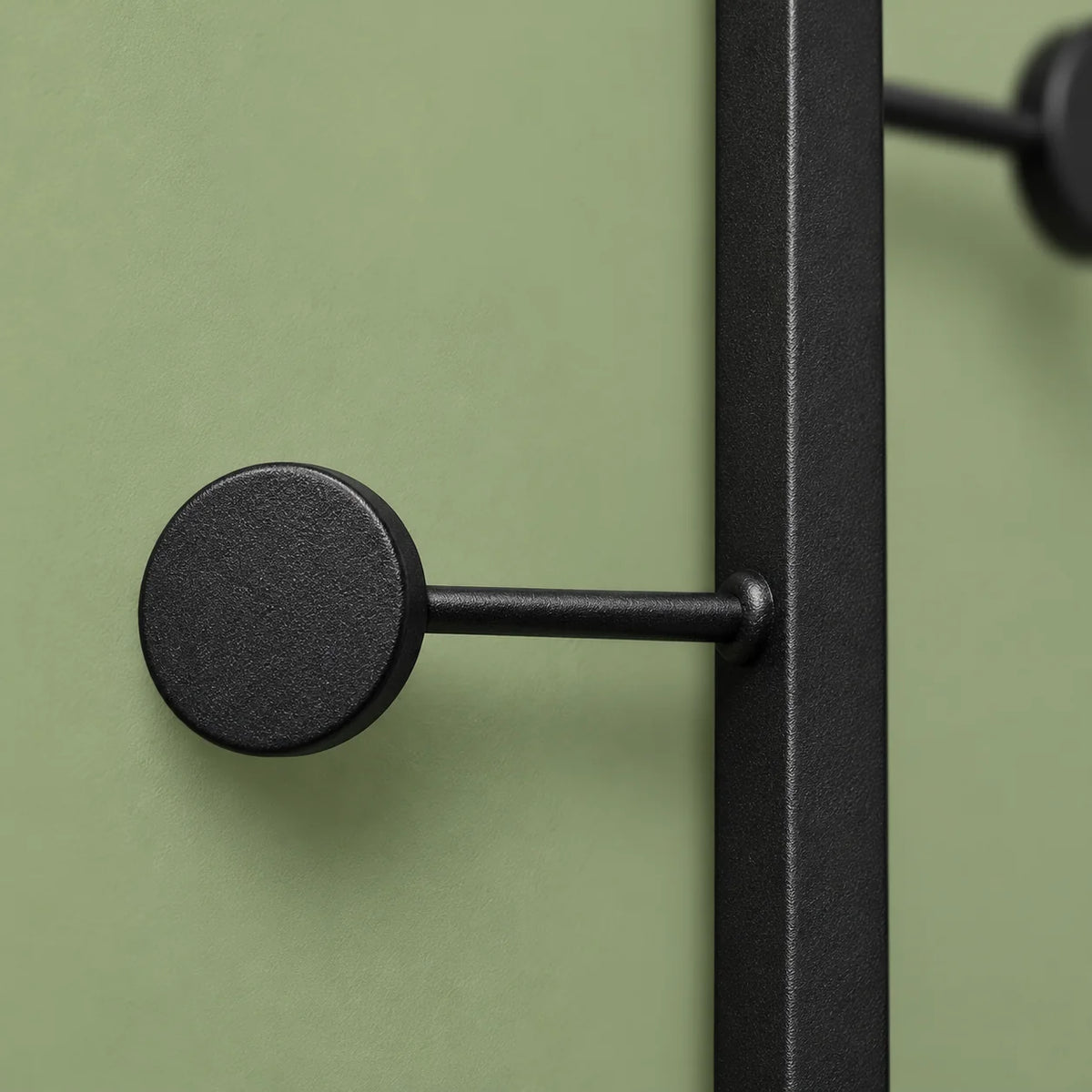 Détail du crochet inférieur rond et de sa tige en métal noir mat sur fond vert sauge
