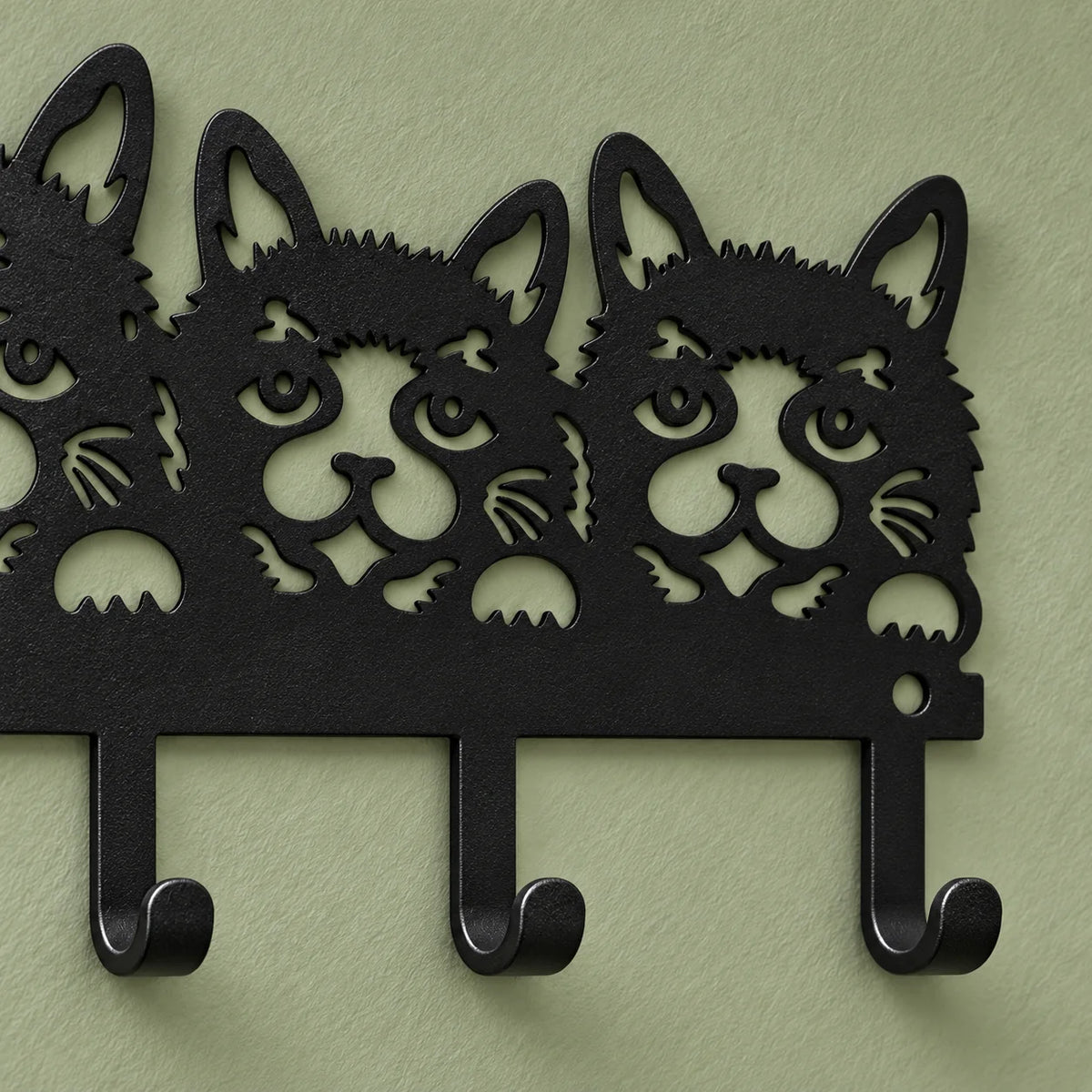 Détail des visages de chats, de la fixation et des crochets du porte-manteau noir sur fond vert