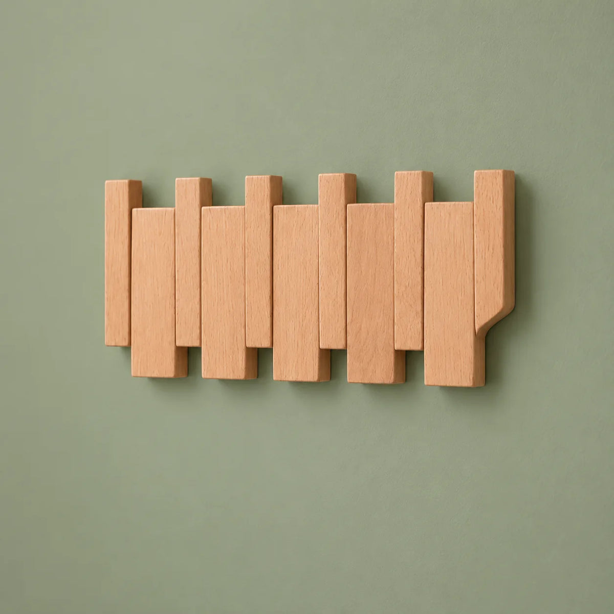 Vue oblique du porte-manteau mural compact en bois clair sur fond vert sauge